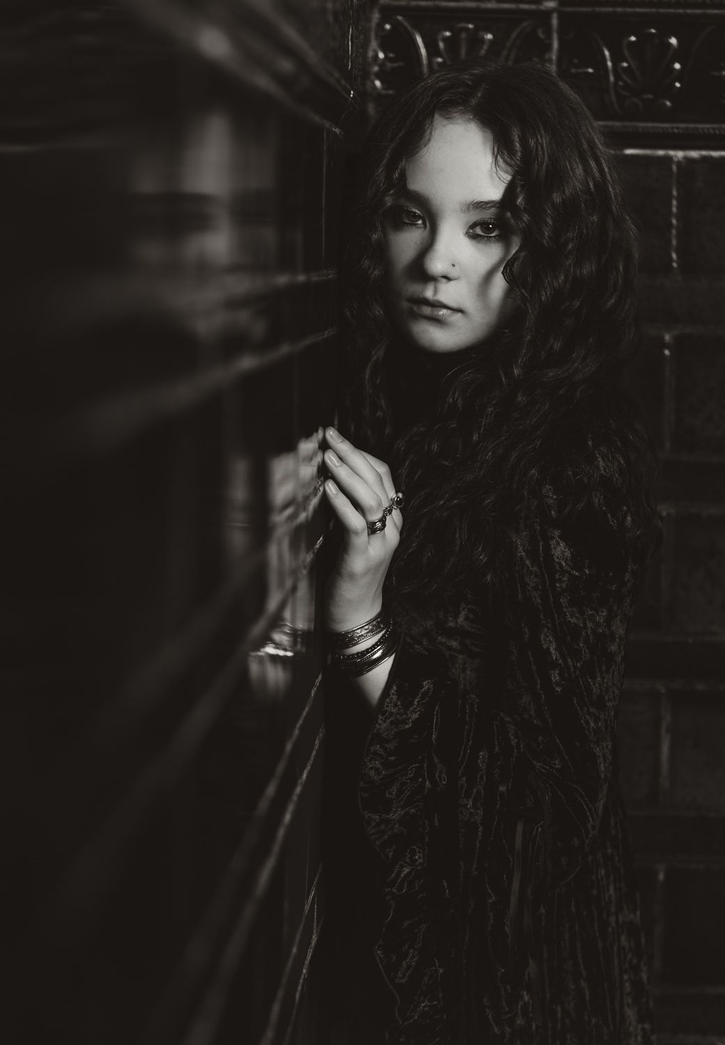 A dramatic black and white portrait of a woman with long dark curly hair against a dark background.