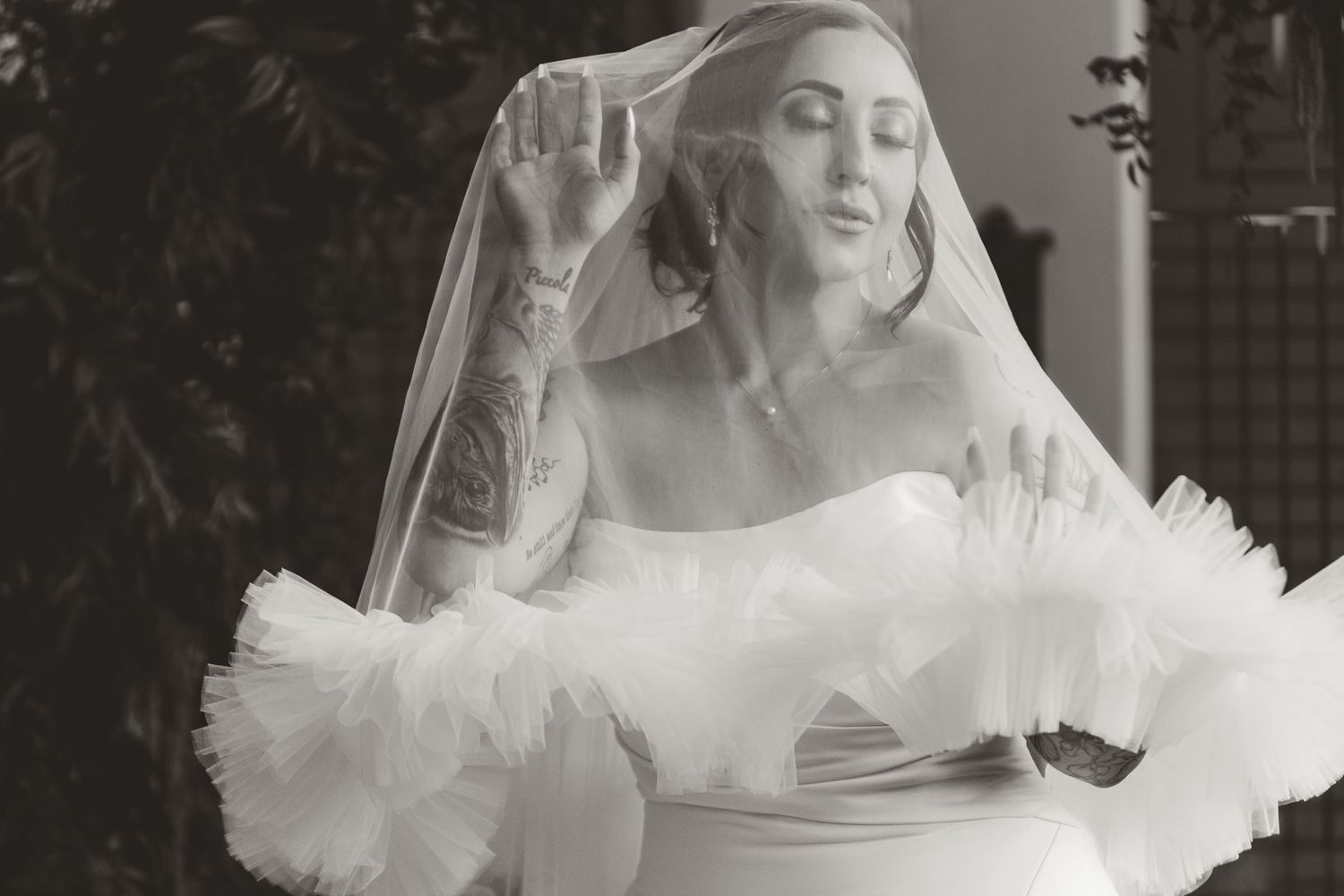 A bride in a dramatic off-shoulder wedding gown with ruffled tulle details poses expressively in black and white.