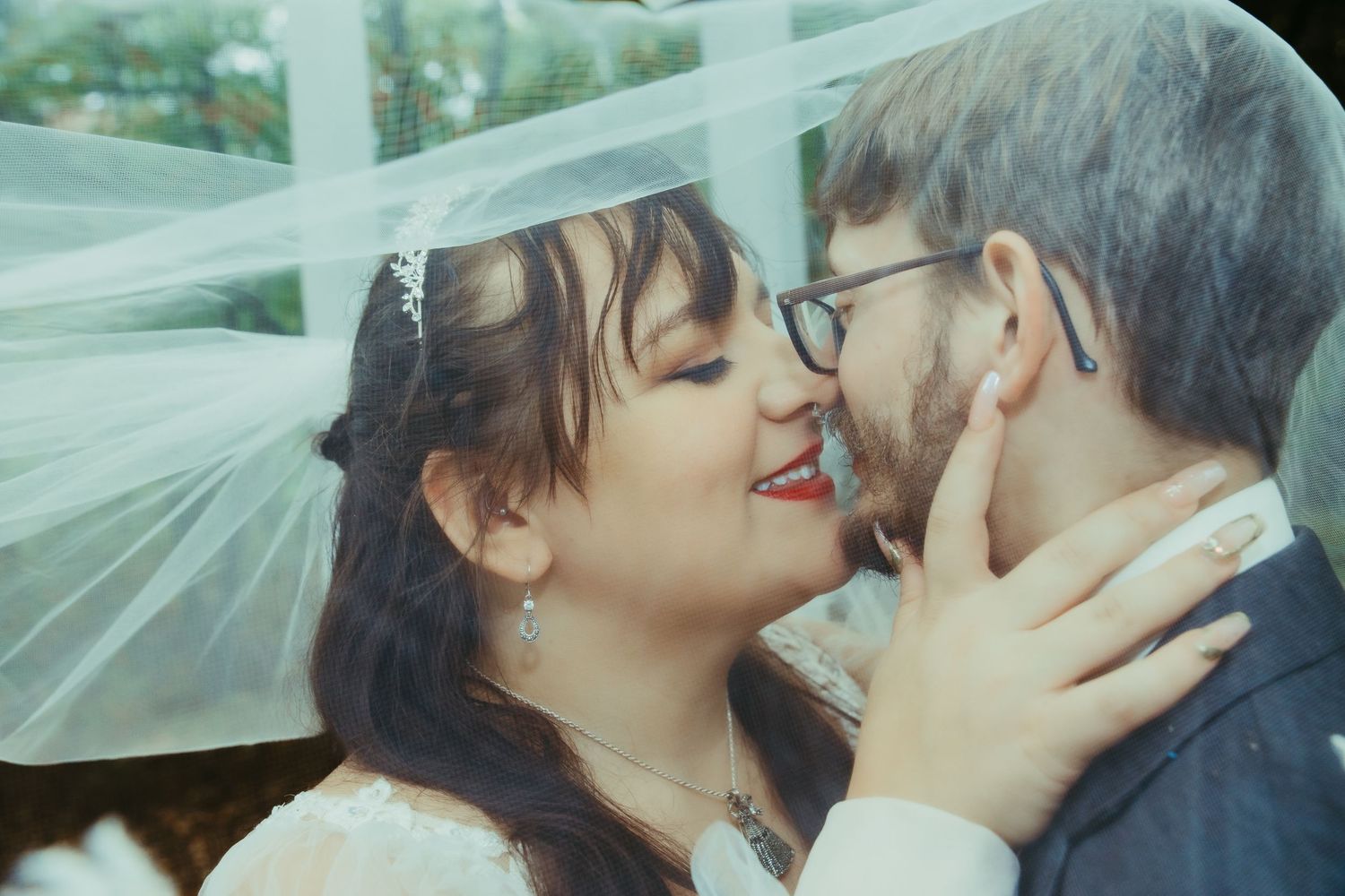 Intimate close-up shot of newlyweds sharing a tender moment under flowing veil on their wedding day.