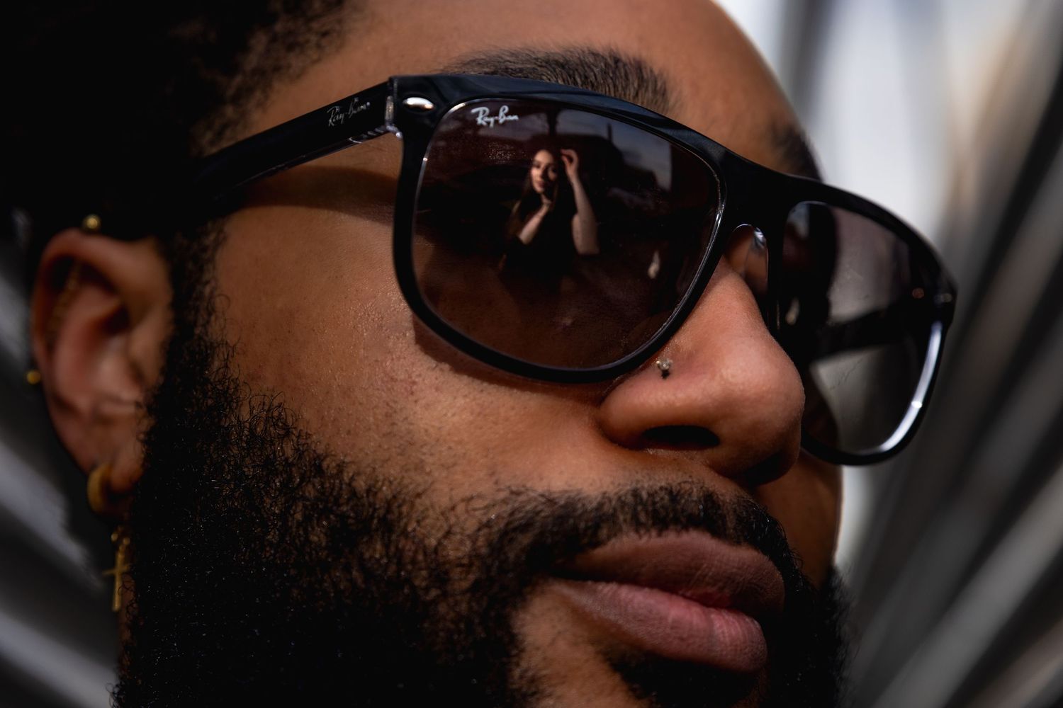 Close up shot showing dark sunglasses reflecting light and a full dark beard against soft lighting.