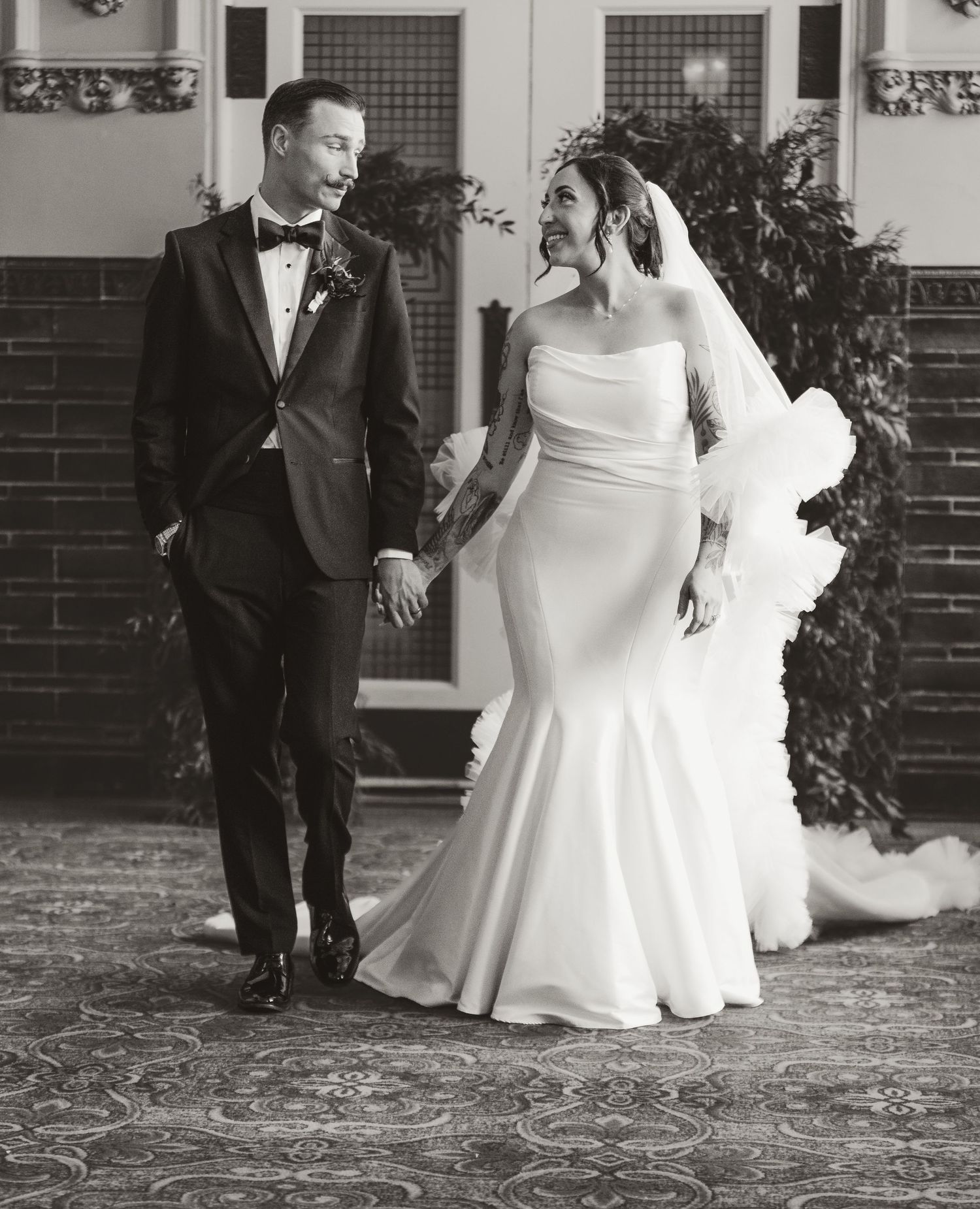 A black and white wedding photograph showing a newlywed couple holding hands and smiling on their special day.