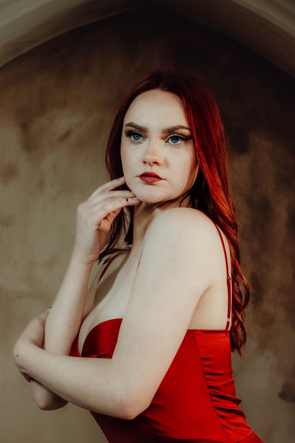 A figure in a red satin dress poses dramatically against a dark textured background in an artistic portrait series.