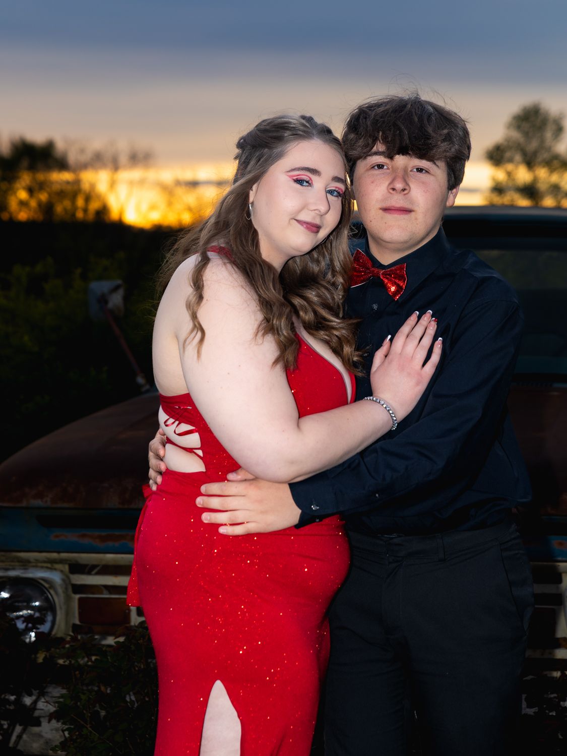 A couple shares an intimate moment at sunset against a darkening sky background.