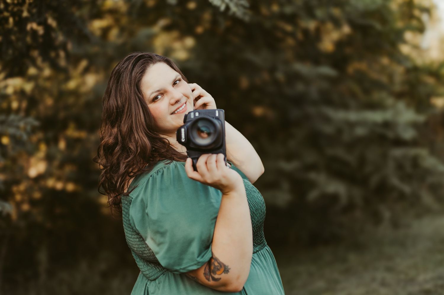 A person in a green dress holds a black cat against a sunset-lit background with autumn foliage.
