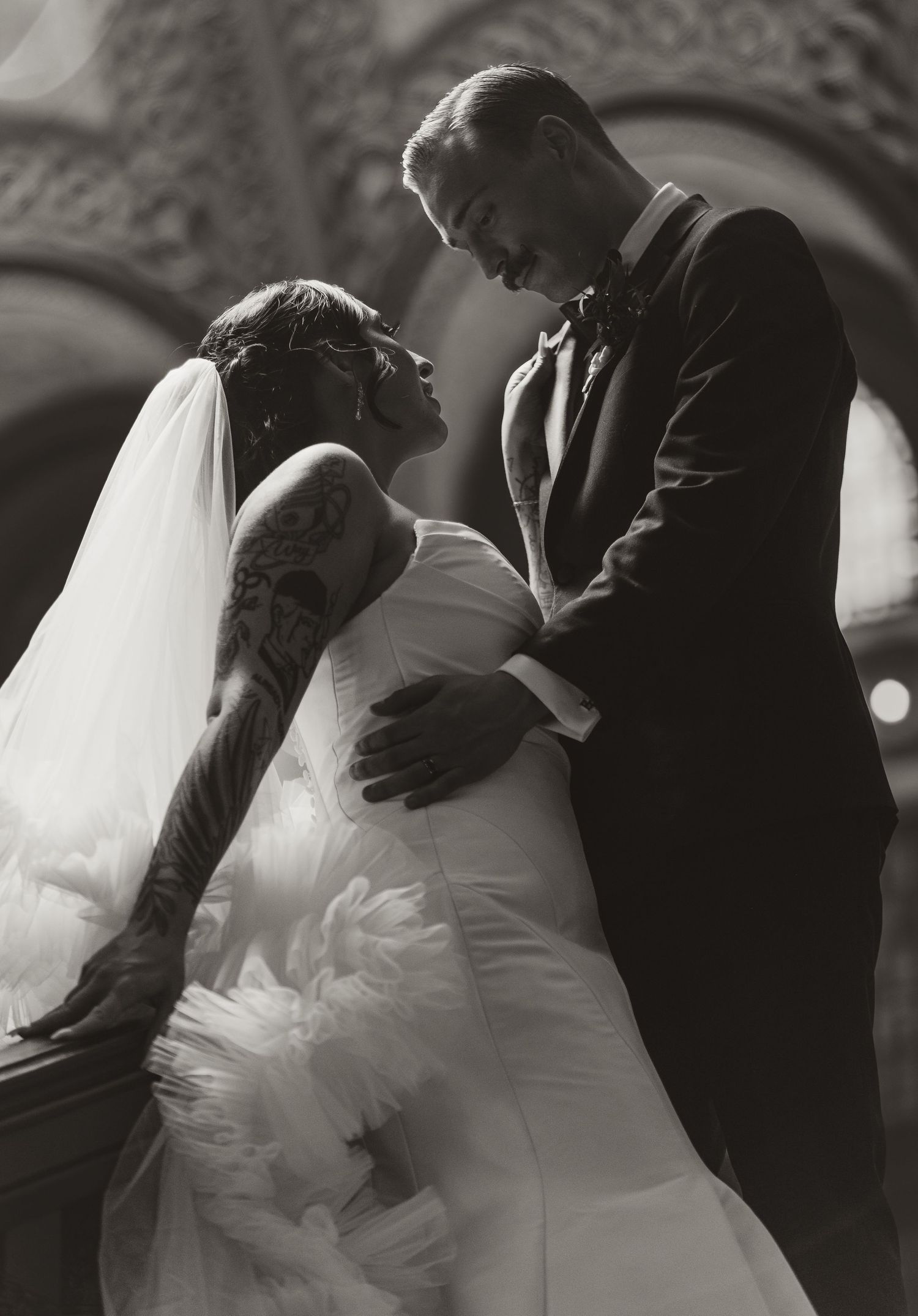 An intimate black and white wedding photograph shows a couple in close embrace, the bride in a white dress and veil.