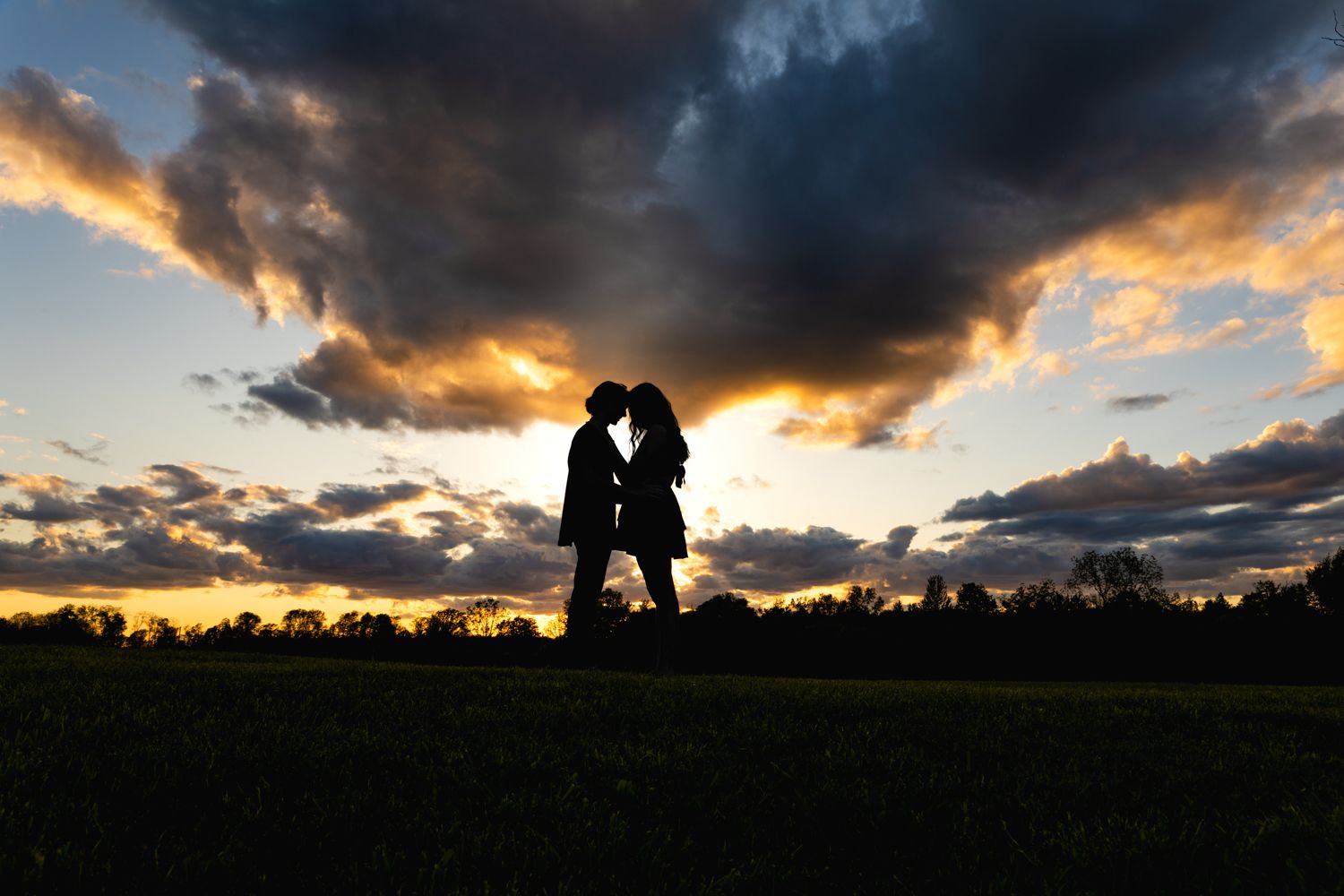 Silhouetted figures stand together against dramatic sunset sky with dark clouds and golden light.