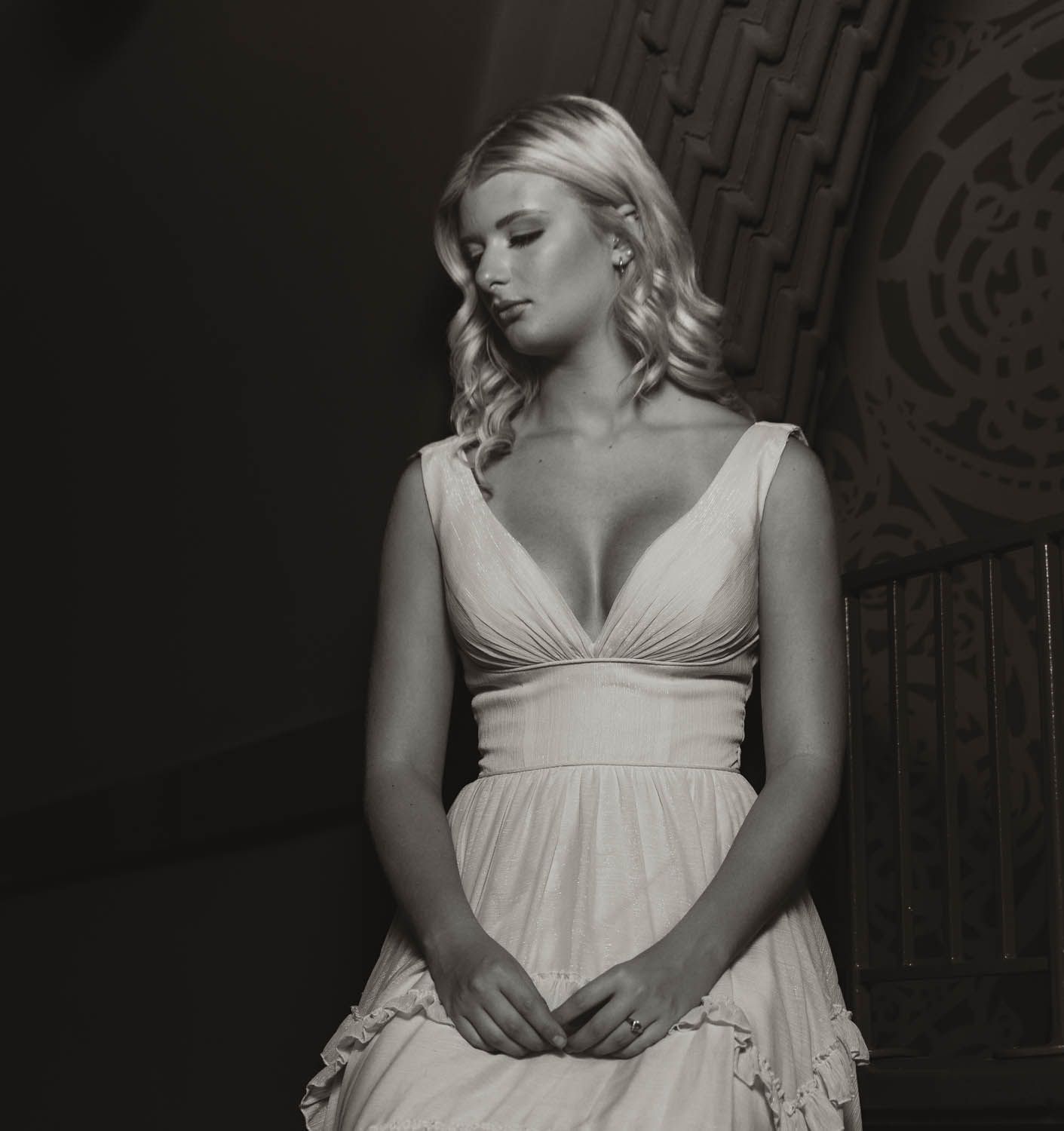 Dramatic black and white portrait of a person in an elegant white dress with plunging neckline against textured background.