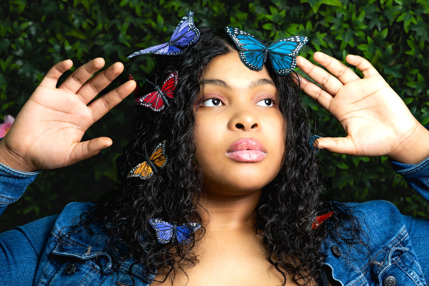 Woman in blue dress poses with colorful decorative butterflies while lying on grass against green foliage background. seniors