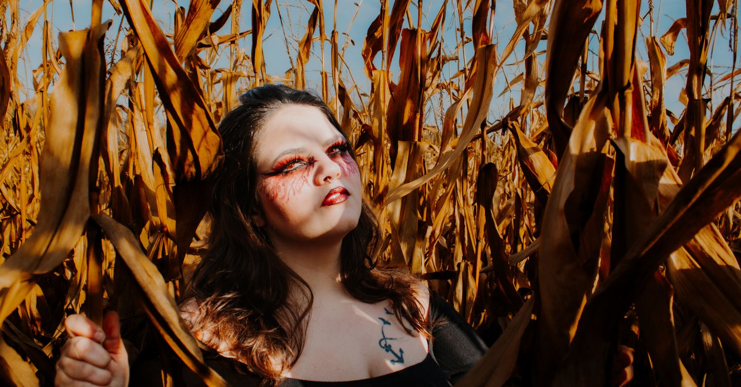 A person standing among golden dried corn stalks in warm autumn sunlight.