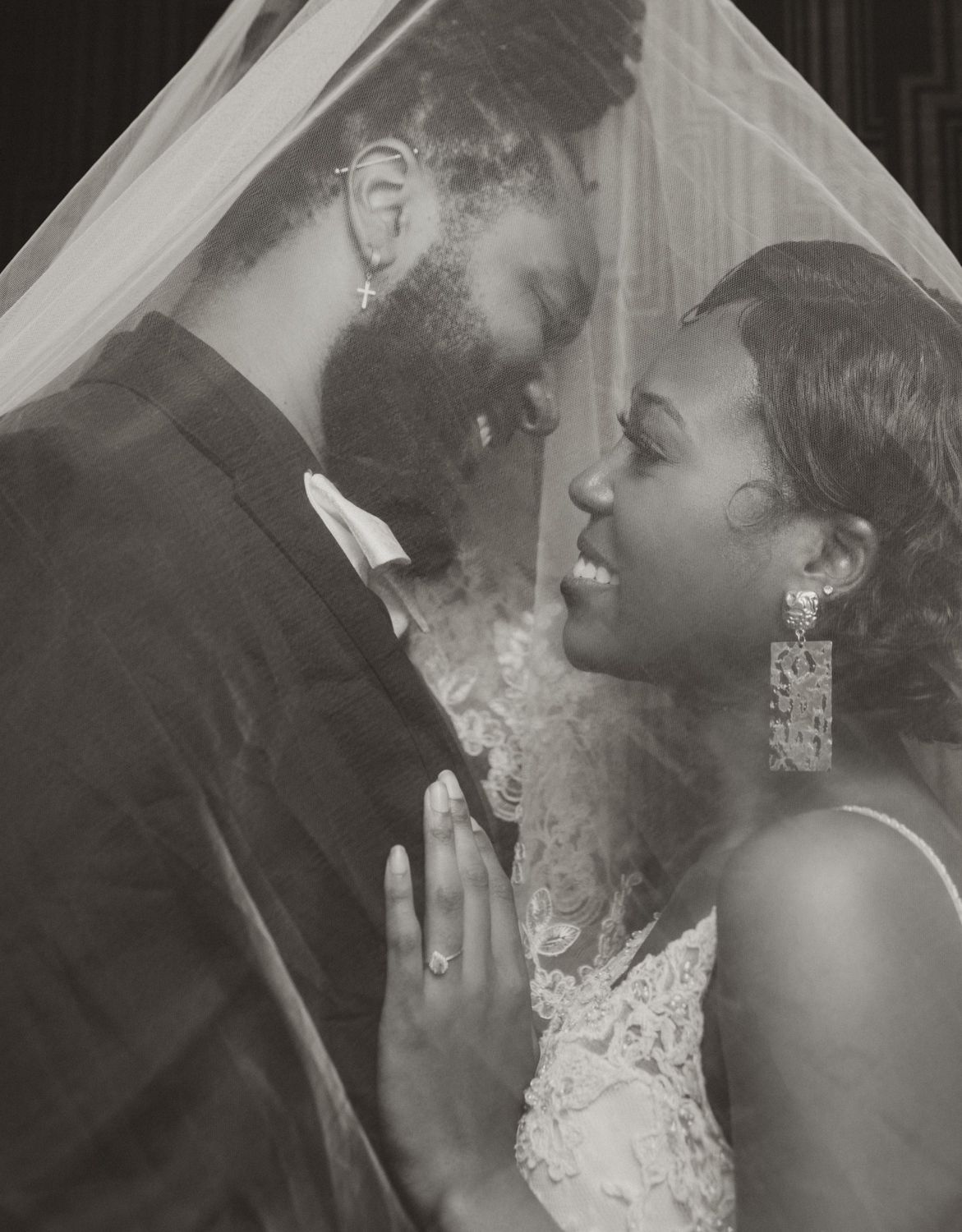 Black and white wedding portrait showing tender moment between newlyweds under veil.