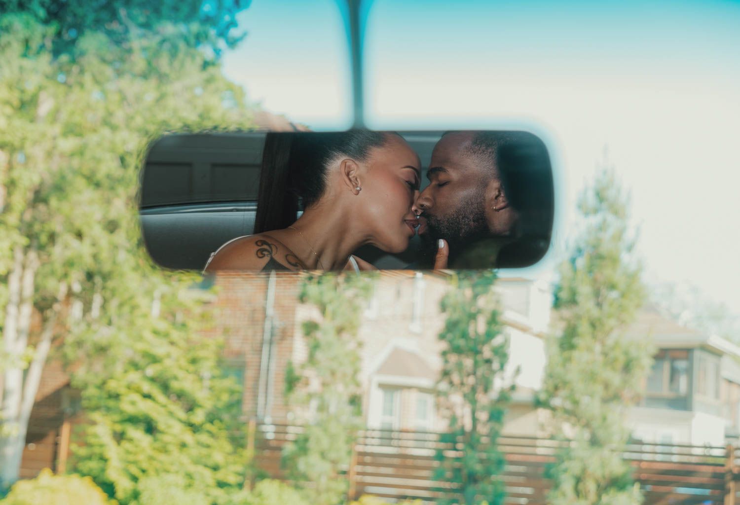 Reflection in rearview mirror shows a tender moment between two people kissing against a sunny outdoor background.