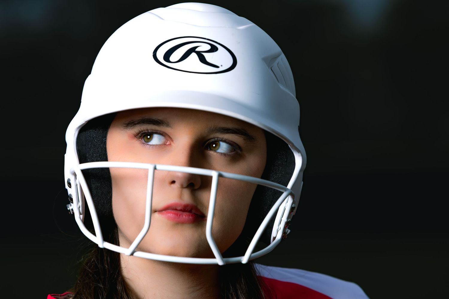 Close-up of white baseball helmet with protective face guard against dark background.