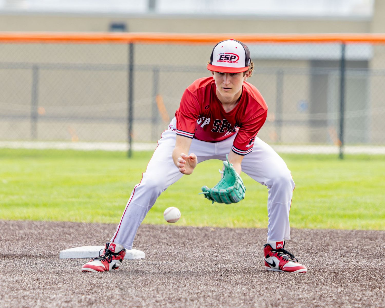 Baseball player in red uniform crouches low on dirt infield waiting for play to start.