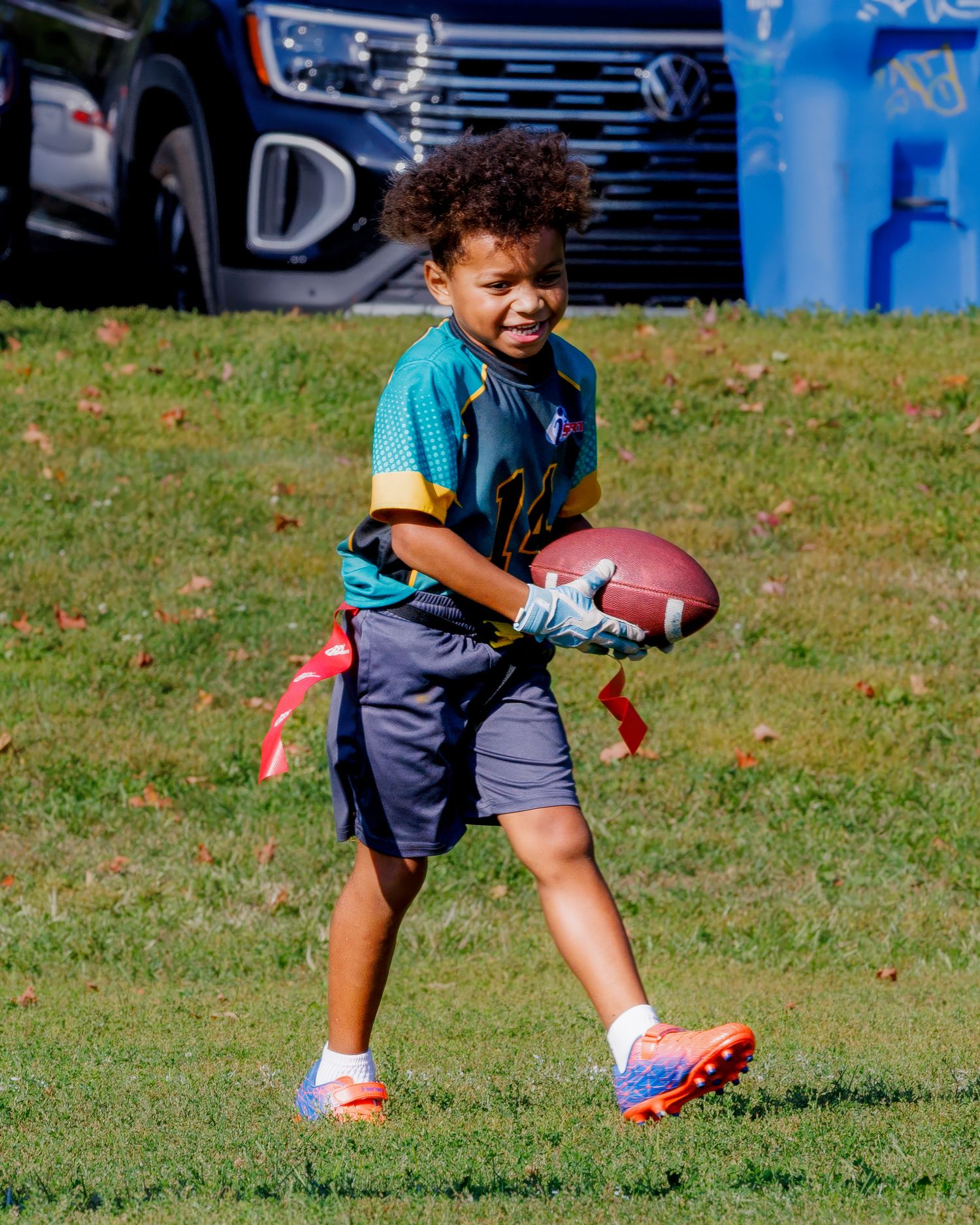 A young athlete practices football drills on a grassy field while wearing a navy and teal uniform.