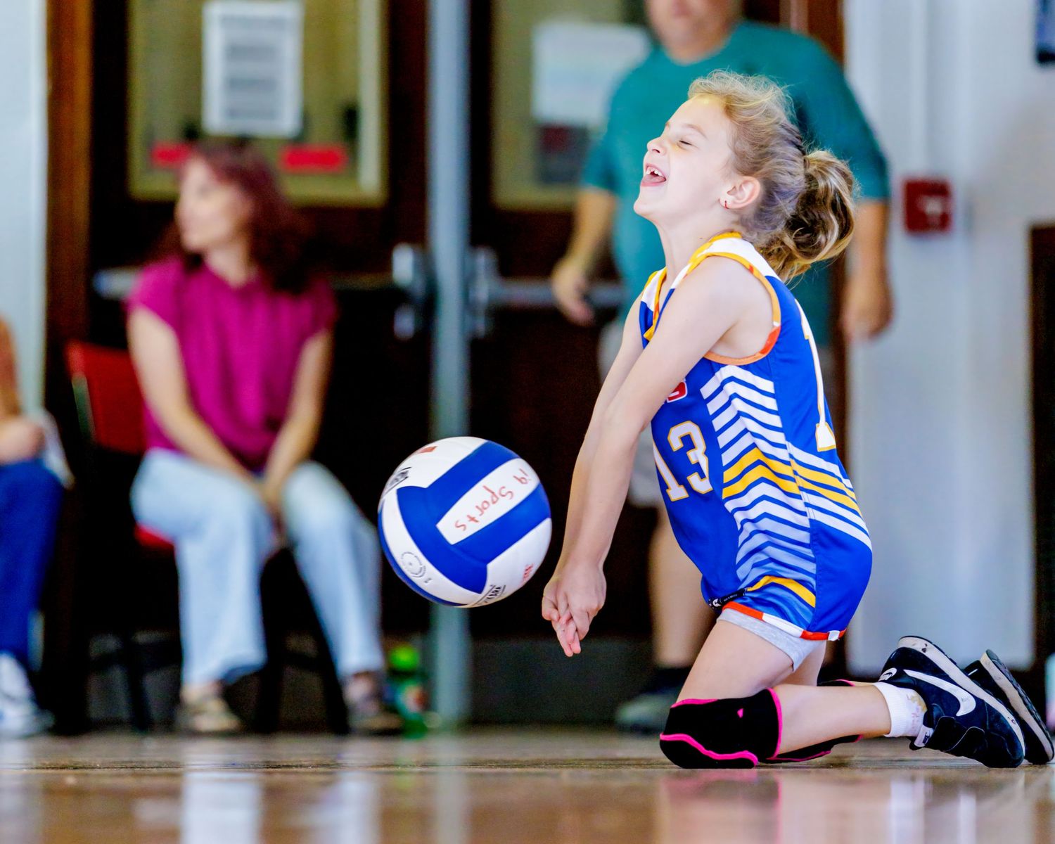 Volleyball players in blue uniforms diving and stretching during an intense indoor match.