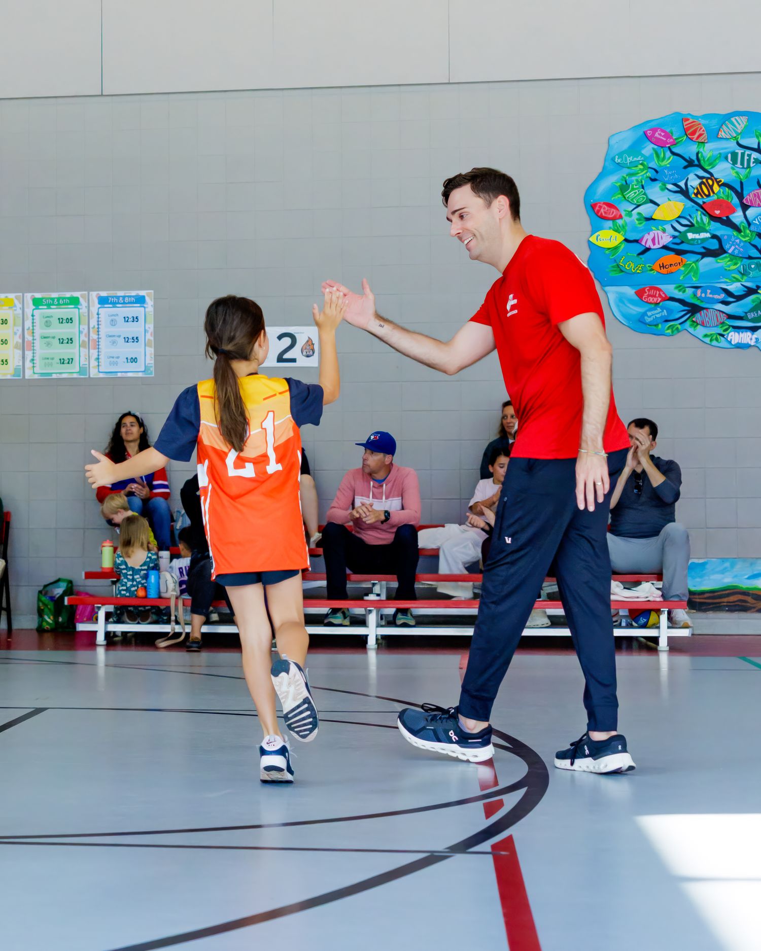 Children practicing basketball drills with instructor in gymnasium with colorful wall mural.