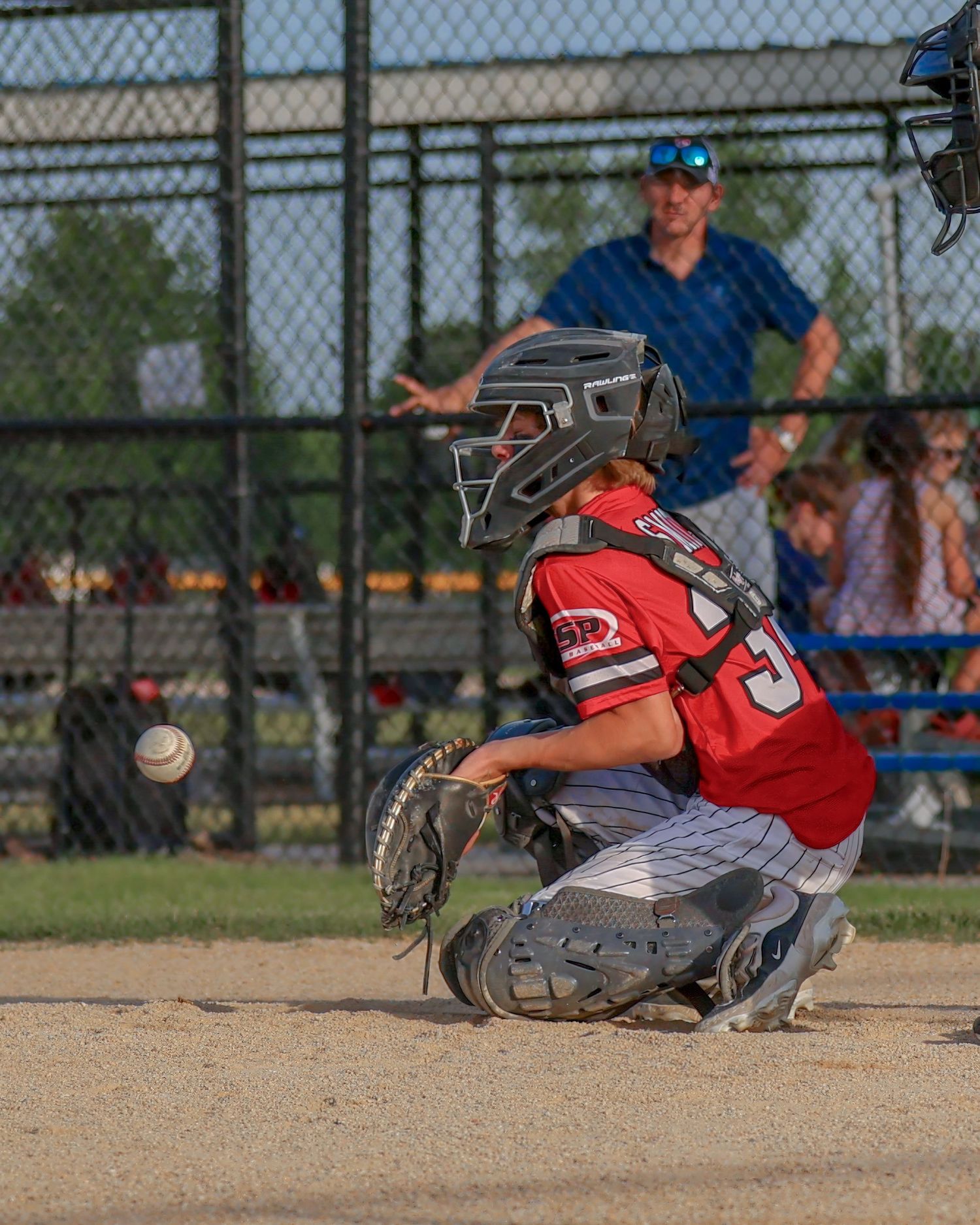 Baseball catcher in red uniform crouches behind home plate during game.
