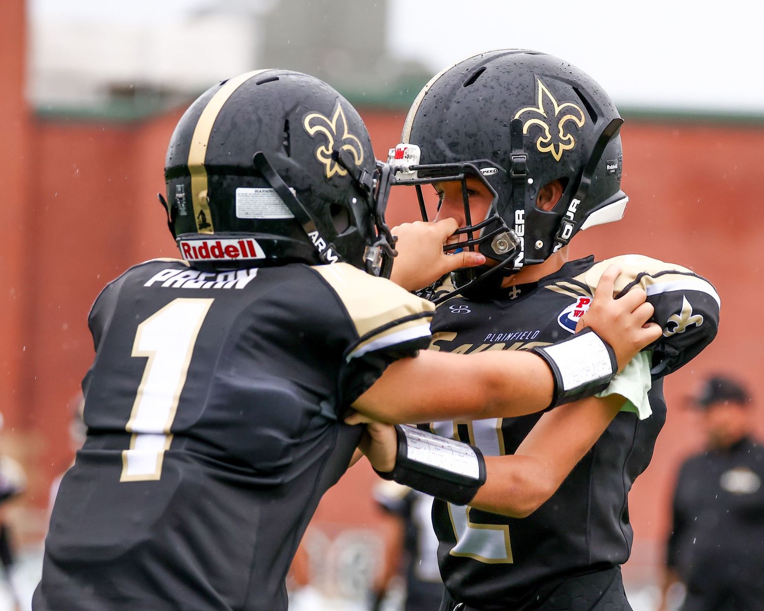 Two youth football players in black Saints uniforms celebrate together during a game.
