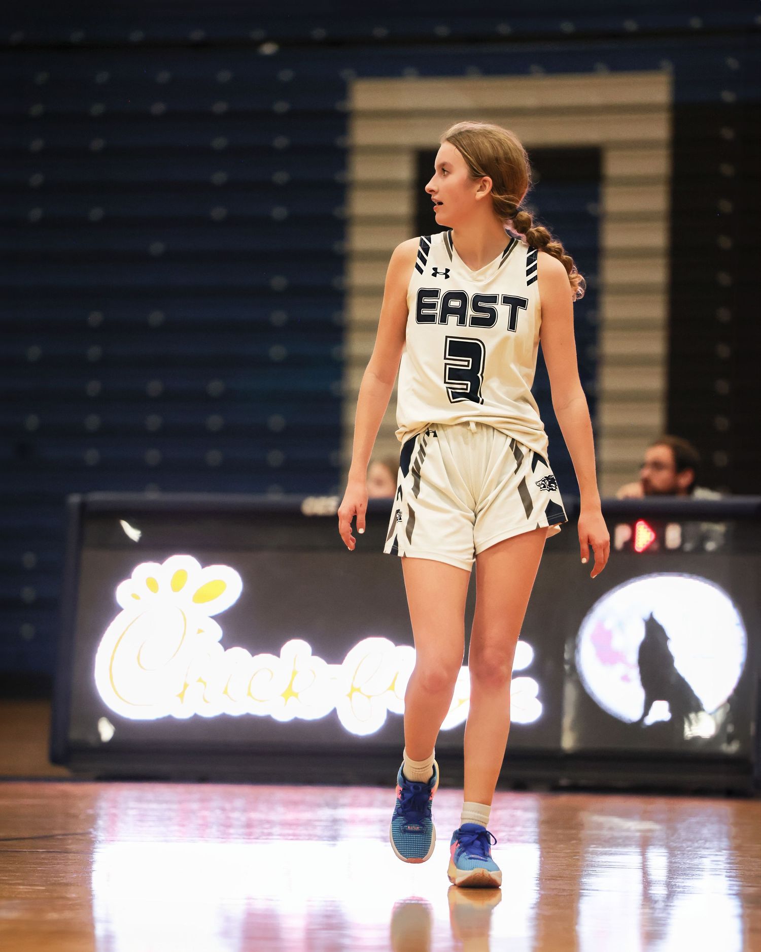 Basketball players in white uniforms compete on a polished hardwood court during an intense game.