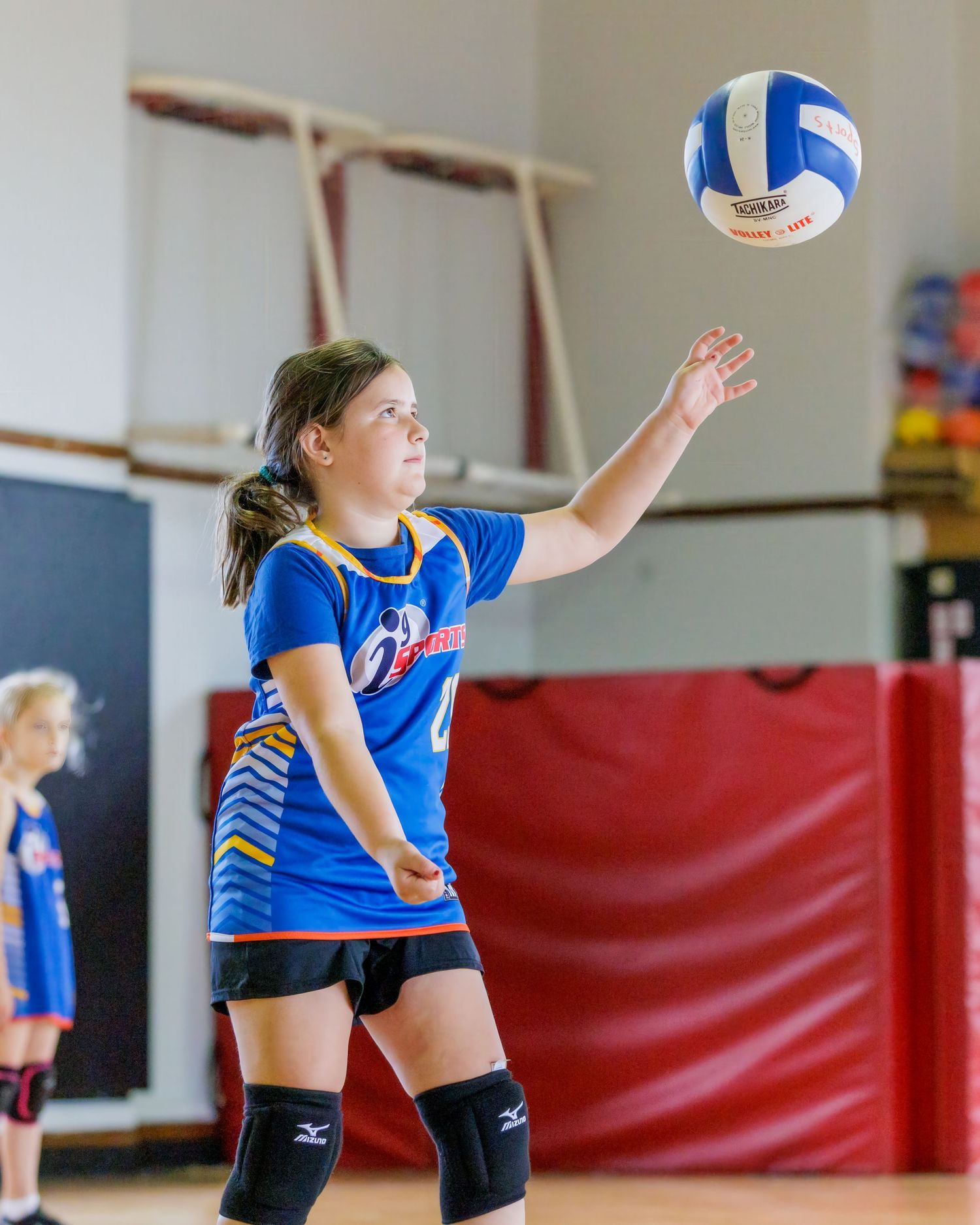Young volleyball player in blue jersey practices defensive stance during indoor training session.