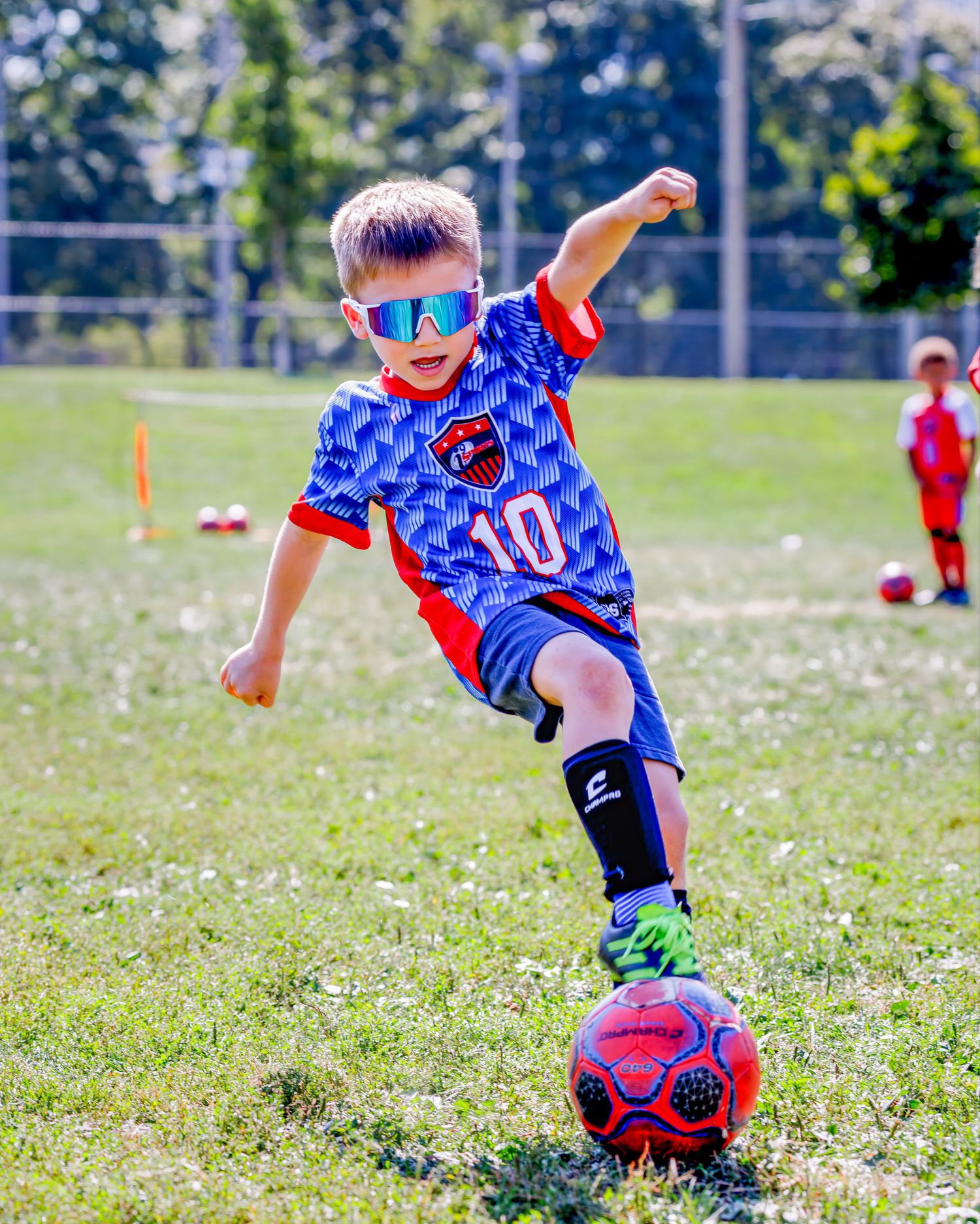Youth soccer players practicing ball skills on grass field wearing blue and red uniforms.