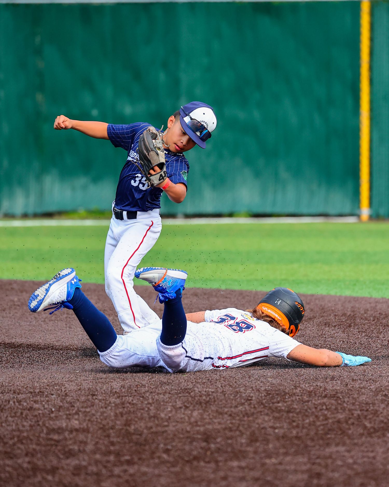 Baseball player slides across dirt infield during intense game play, creating dramatic action sequence.