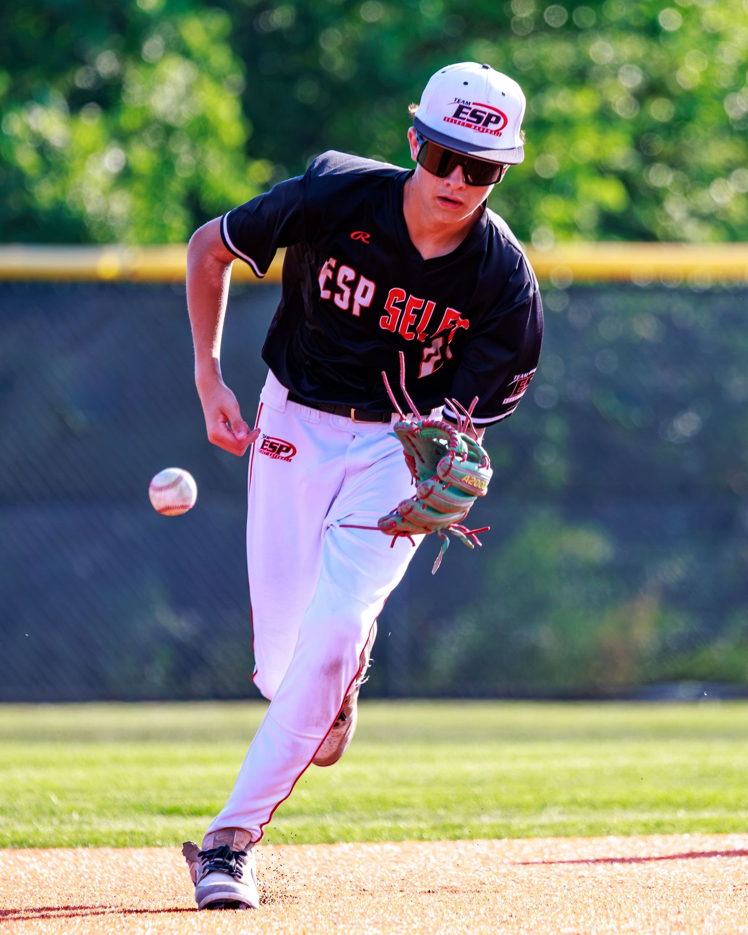 Young baseball player in ESP Select uniform fielding a ground ball during a sunny outdoor game.