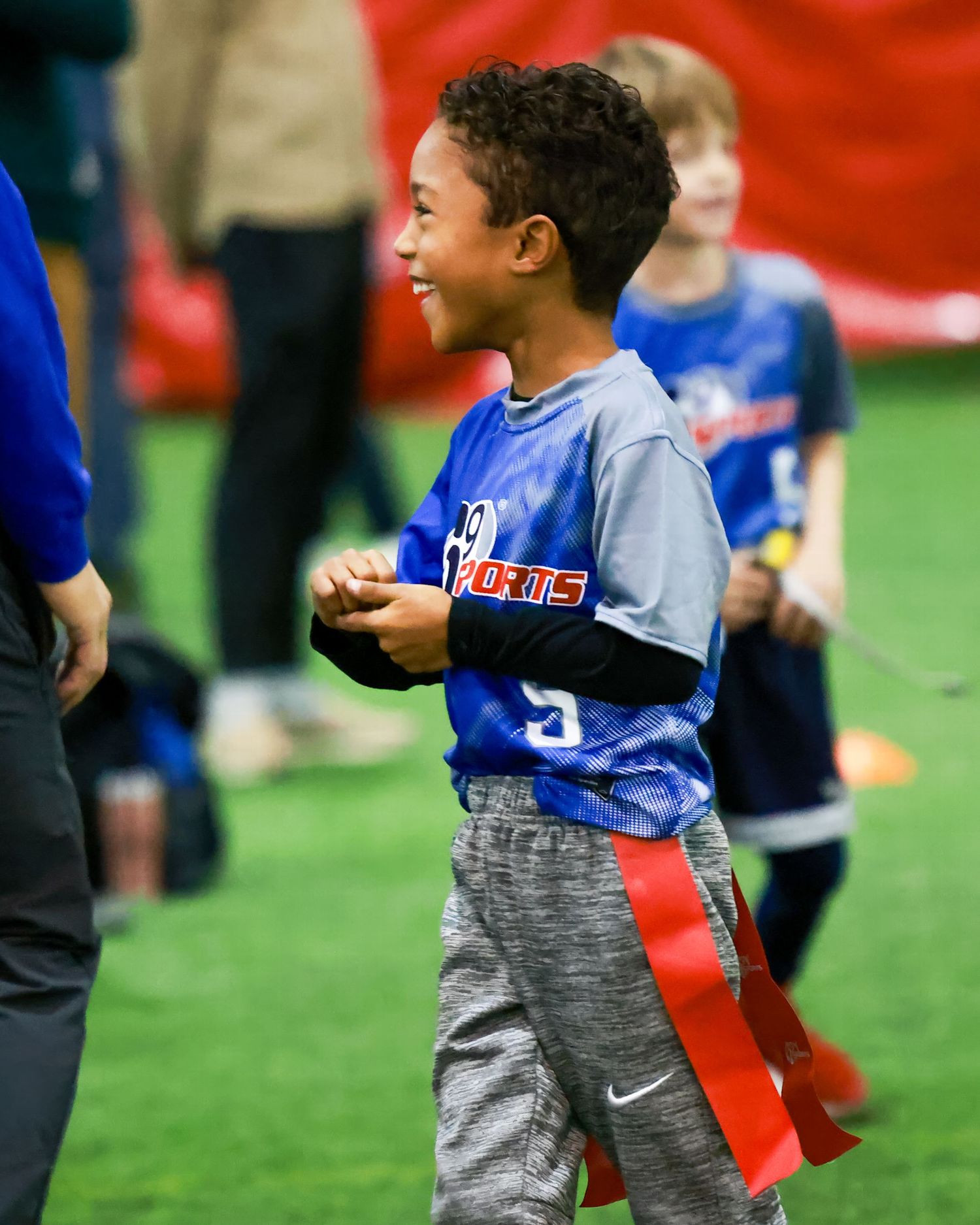 Youth sports player in blue jersey smiles during indoor flag football game.