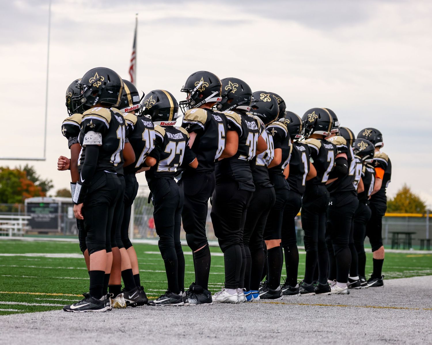 Football players in black uniforms line up on field during national anthem ceremony.