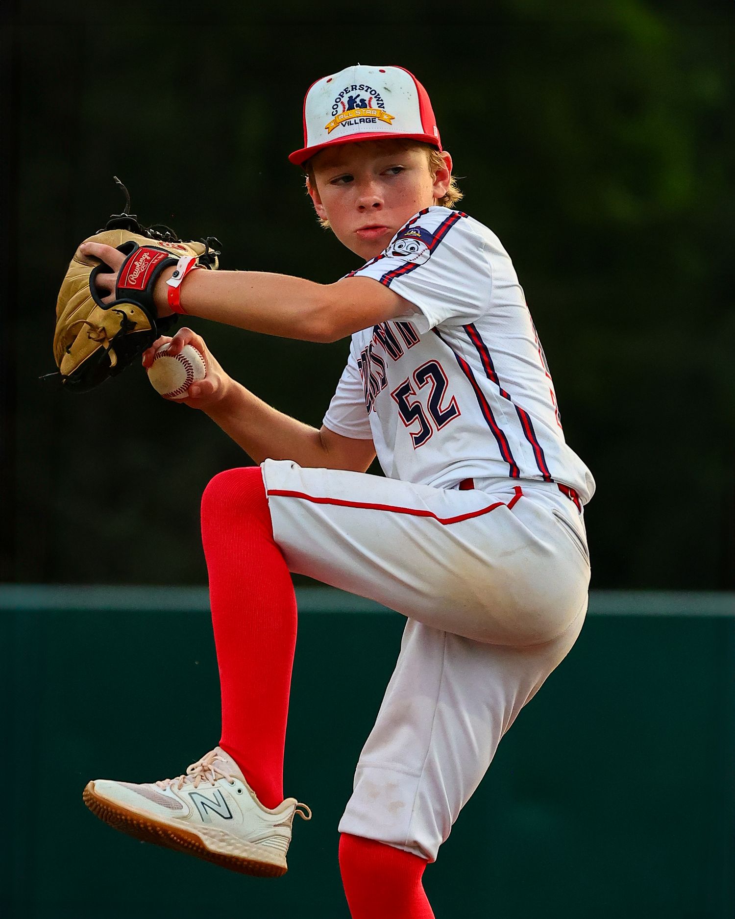 Baseball pitcher in white uniform and red cap winds up to throw during a game on green field.