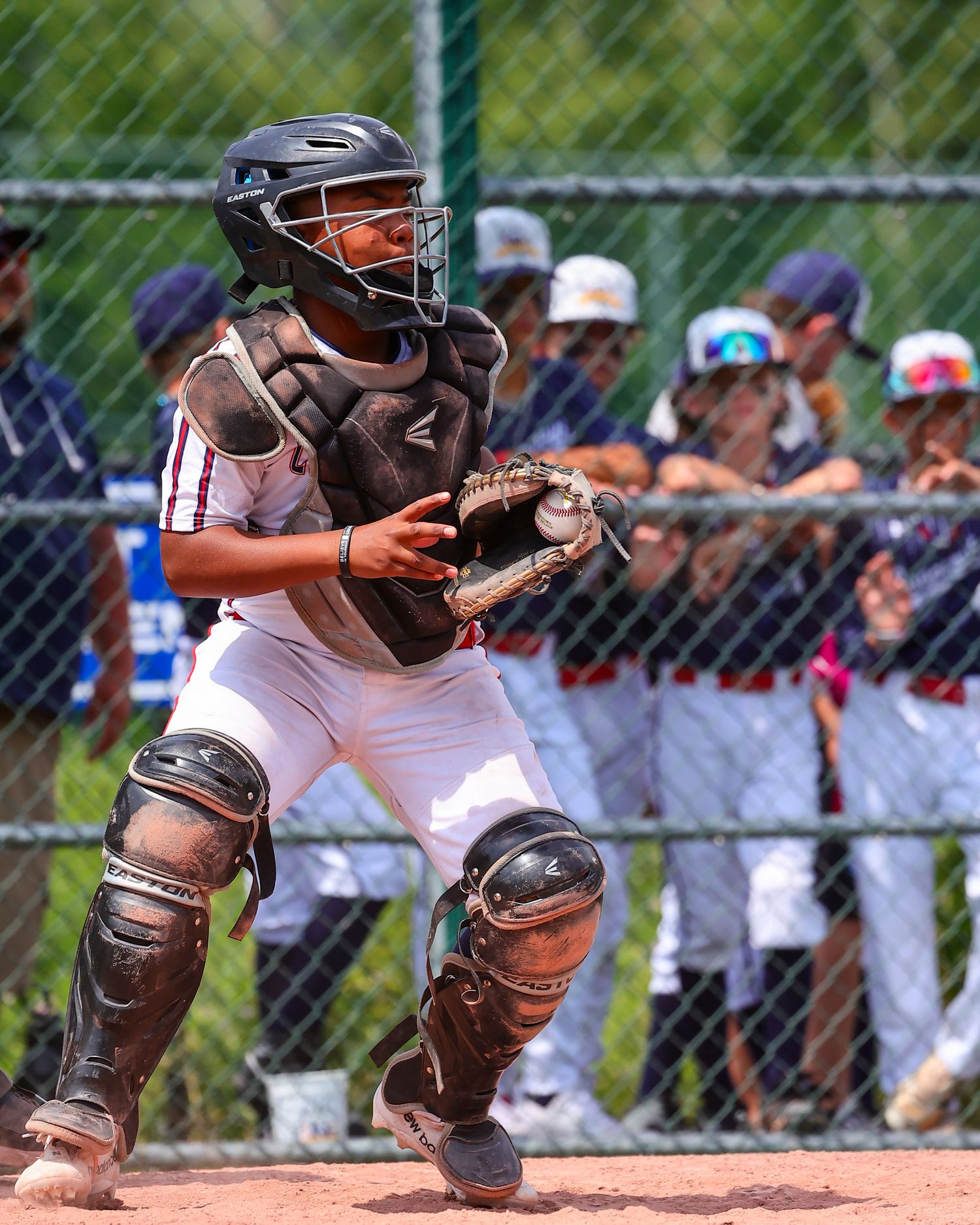Baseball catcher in protective gear crouches in ready position behind home plate during game.