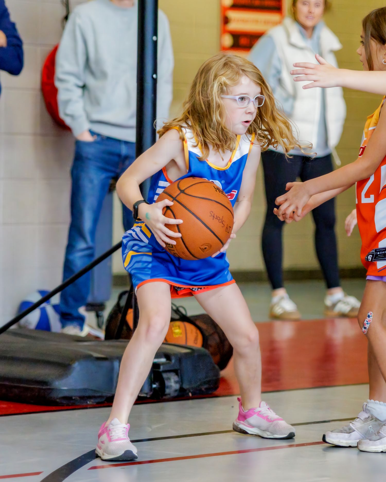 Young girl in blue basketball uniform dribbles ball during youth league game indoors.