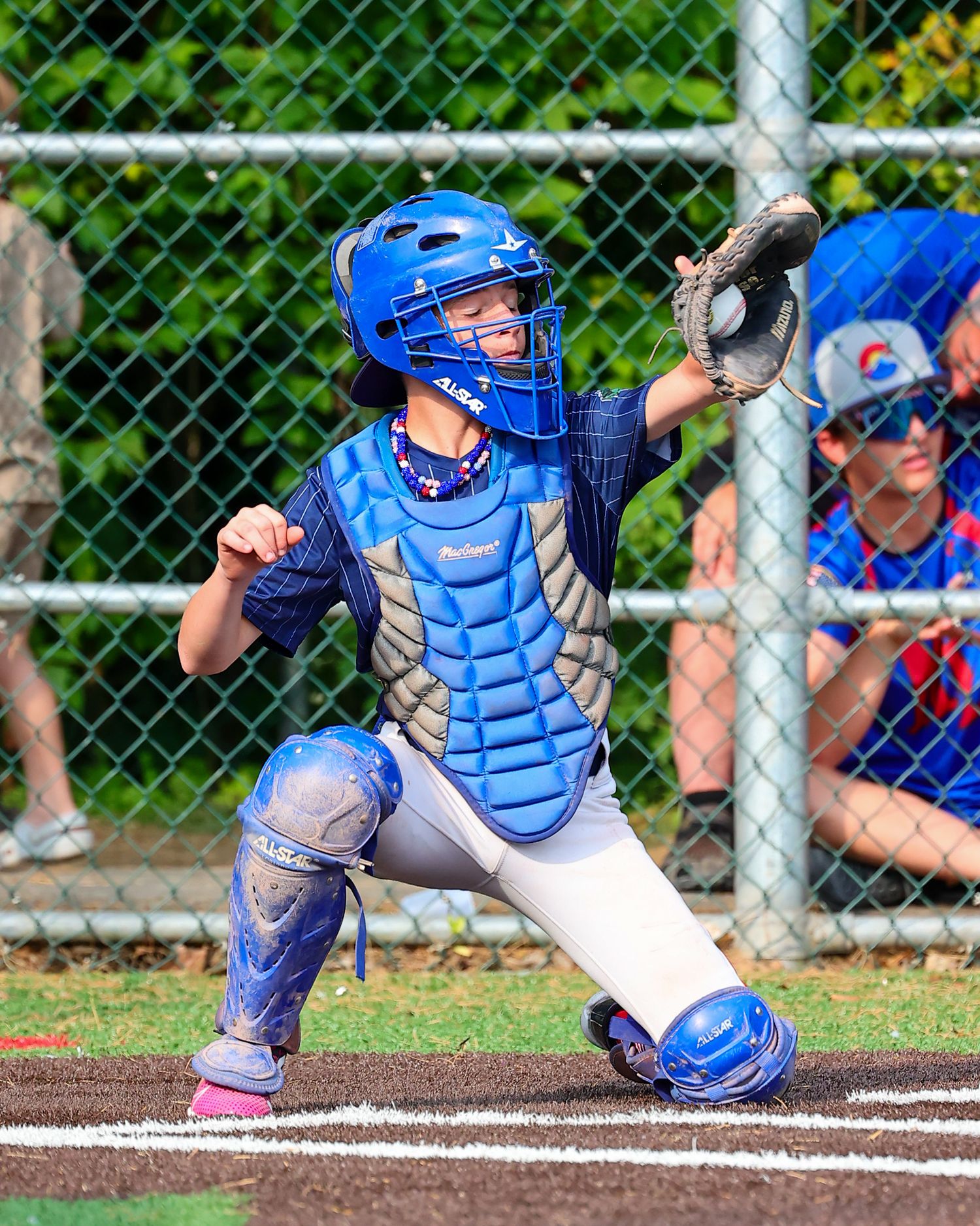 Baseball catcher in bright blue gear crouches in defensive position behind home plate during a game.
