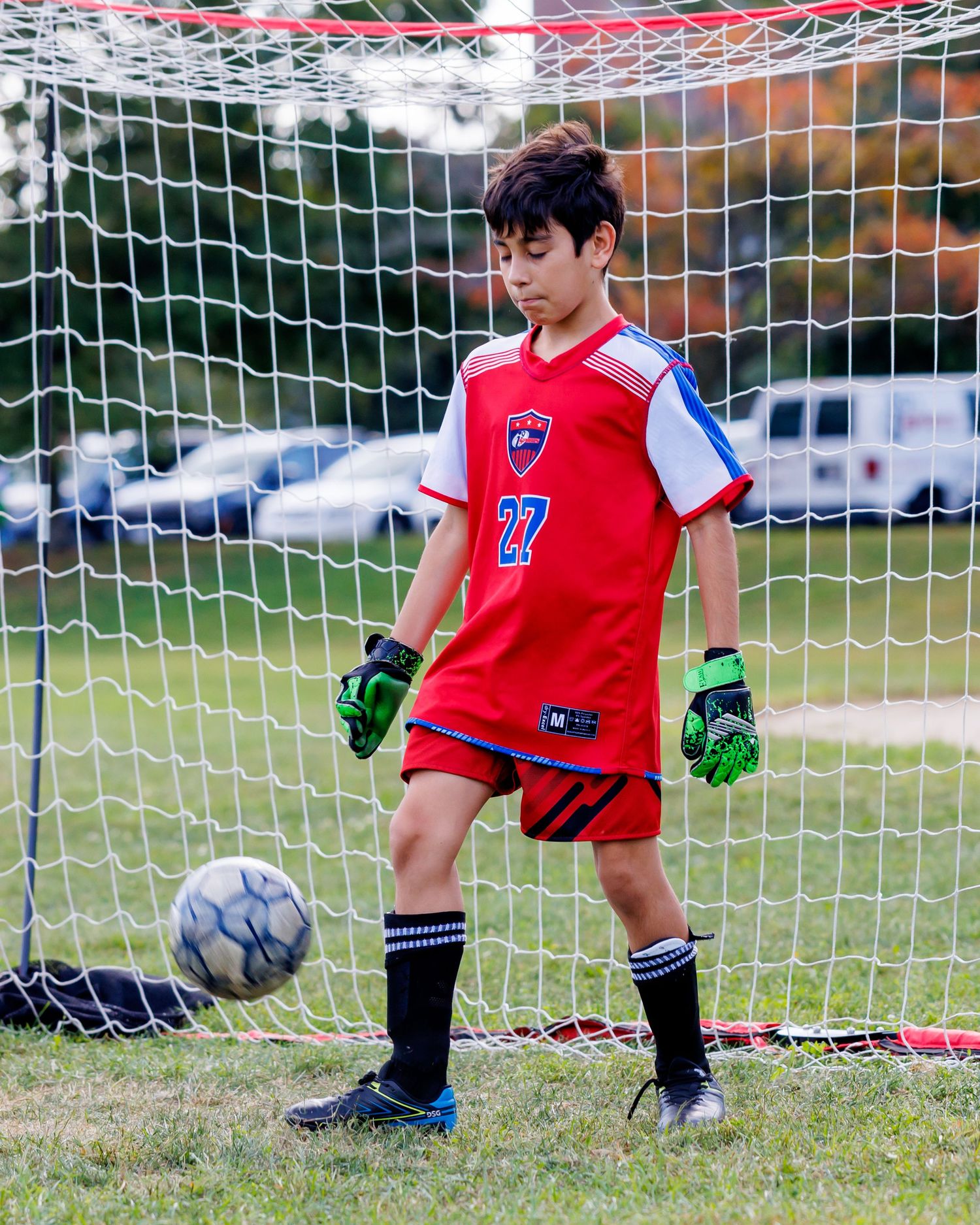 Youth soccer goalkeeper in red uniform practicing saves at the goal net during training.