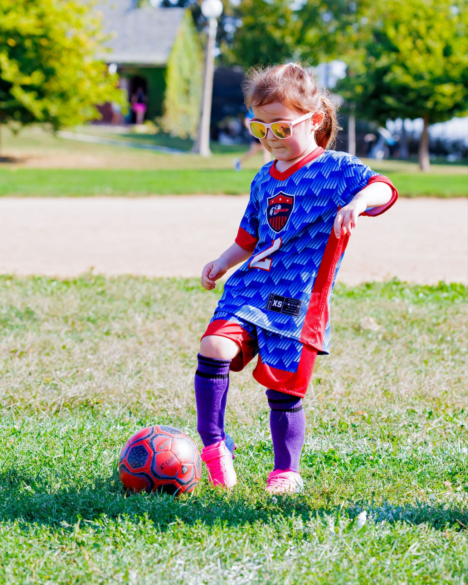 Young soccer player in blue and red jersey practicing ball control on a sunny grass field.