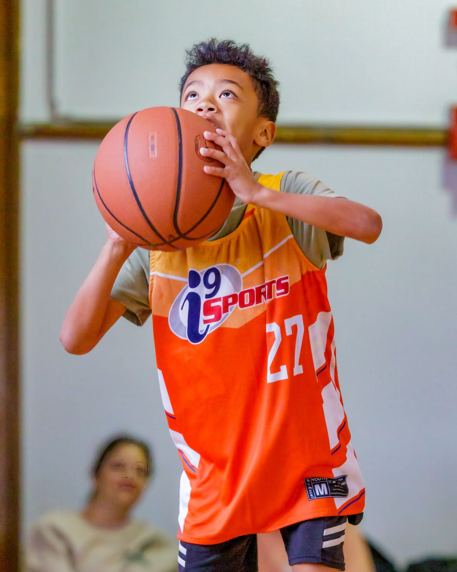Youth basketball players in orange jerseys practicing dribbling skills in indoor gym.