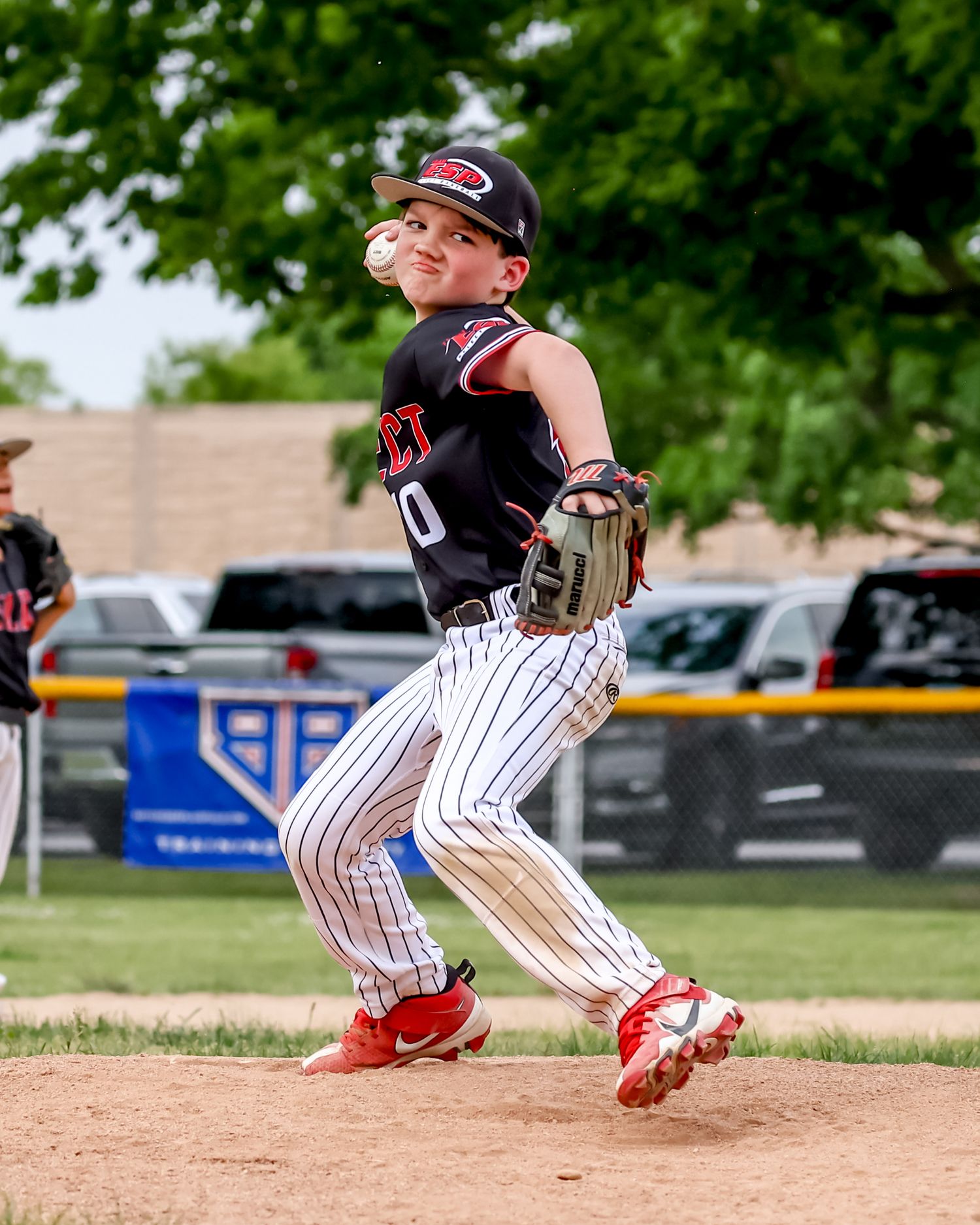 Youth baseball player in pinstriped uniform slides into base during a close play on the baseball field.