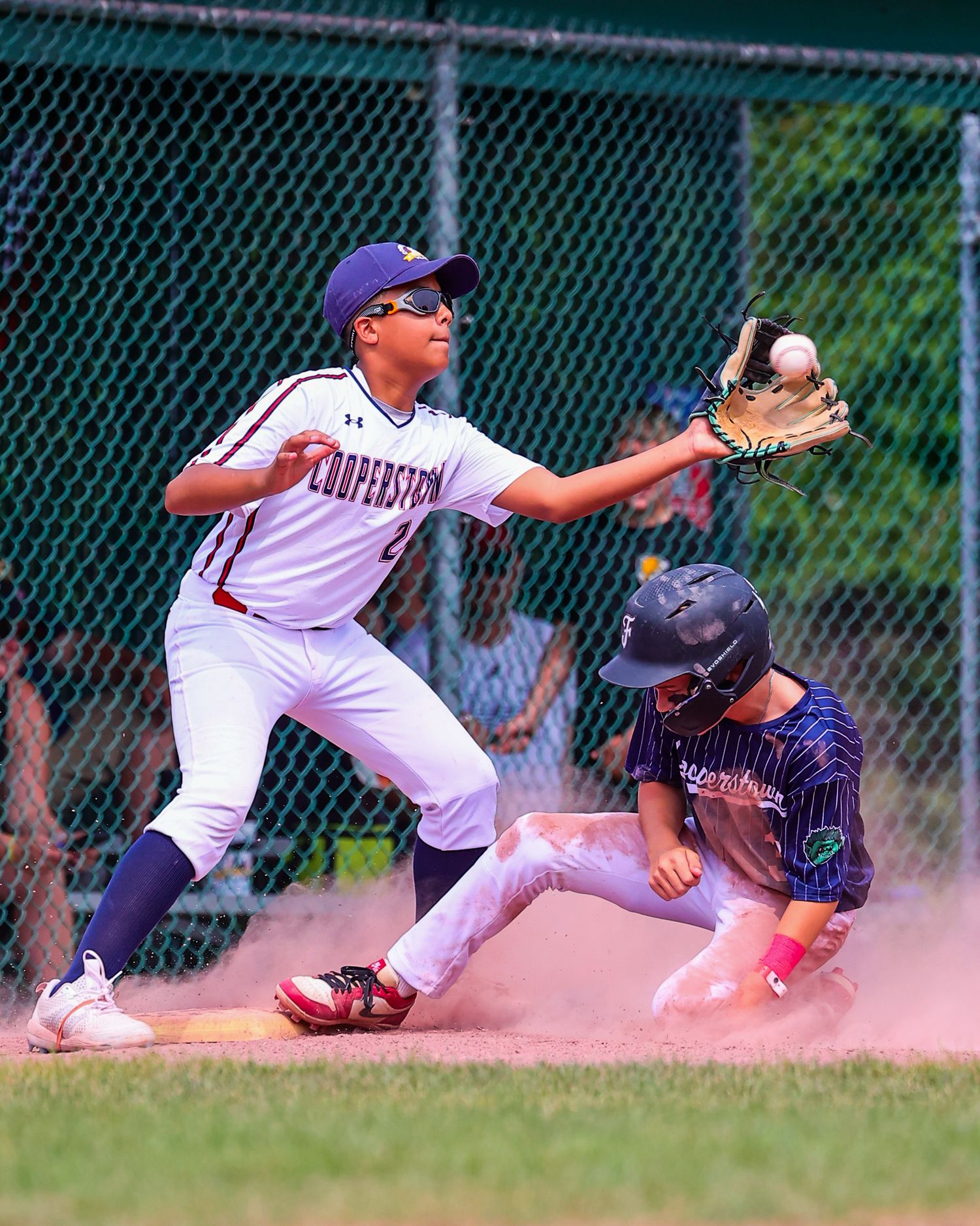A baseball player slides into base as dust kicks up while the baseman attempts to make the tag during a close play.