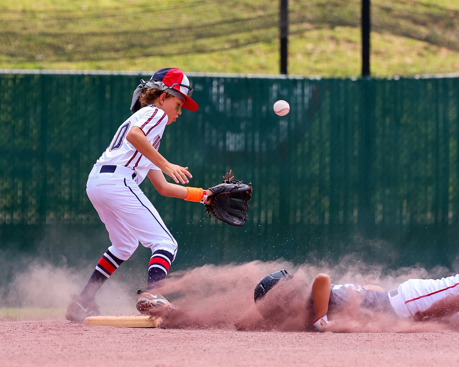 Baseball player slides into base creating a cloud of dust during intense game action.