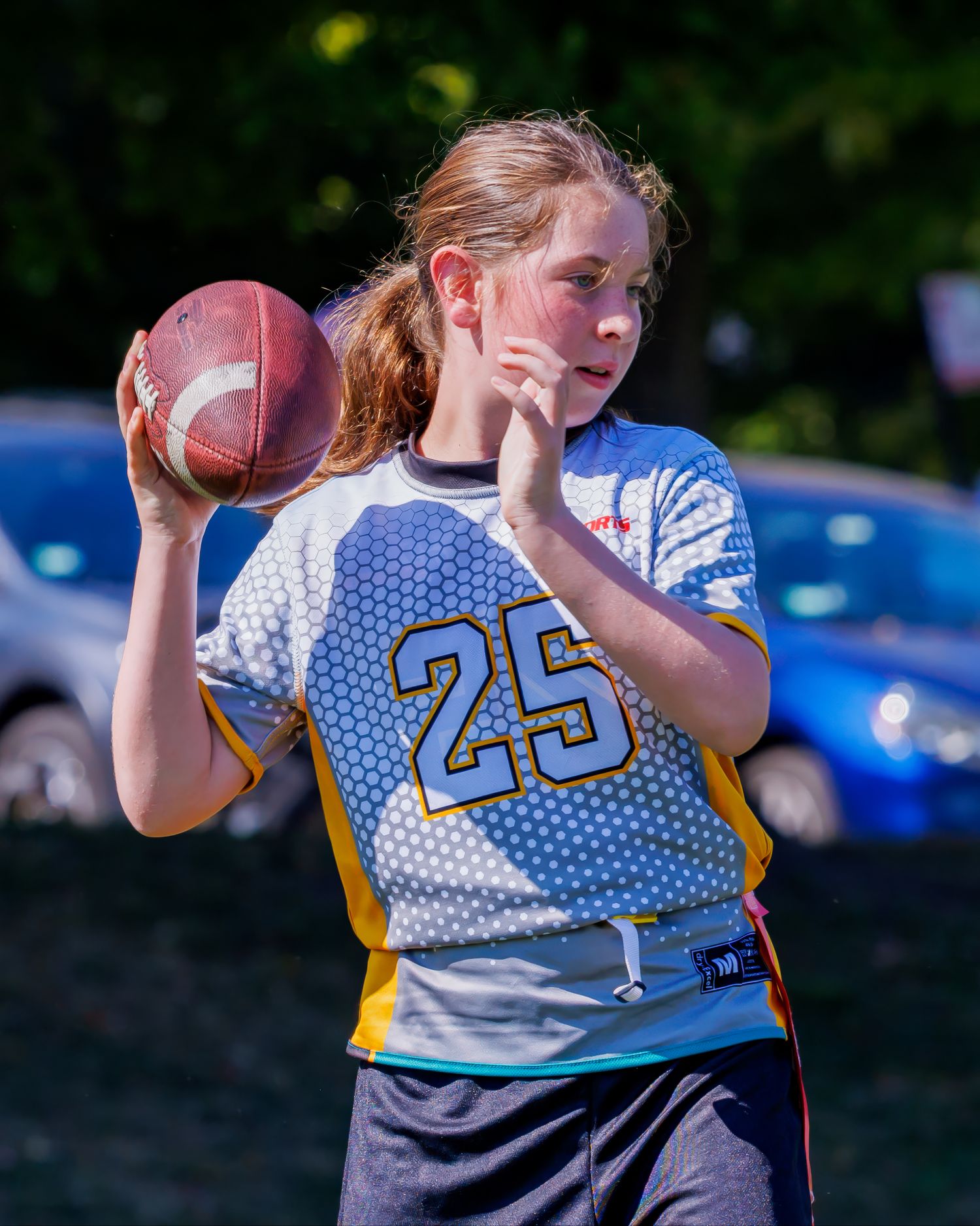Youth athlete in white jersey number 25 prepares to throw football during outdoor game.