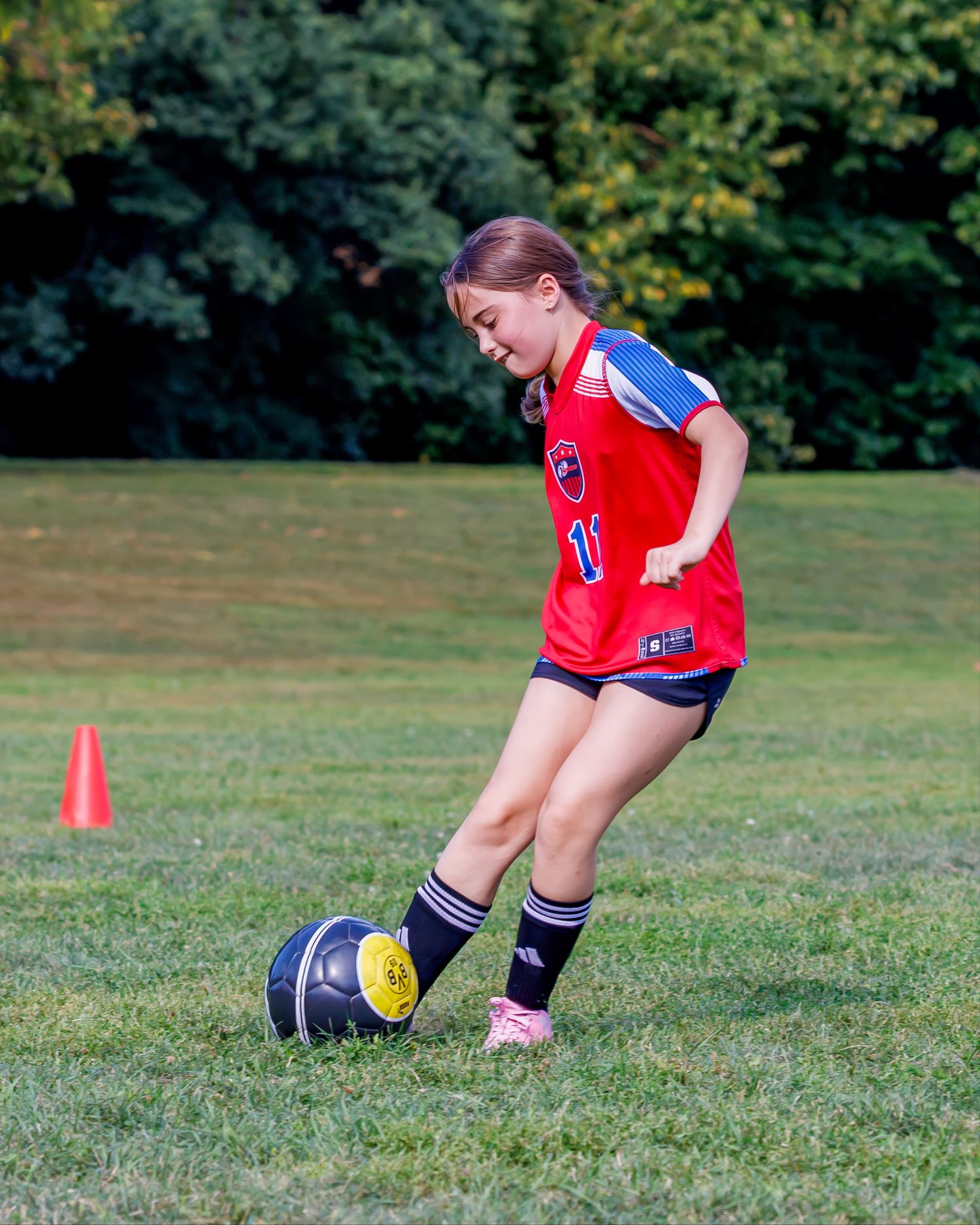 A soccer player in red jersey practices ball control techniques on a grassy field during training.