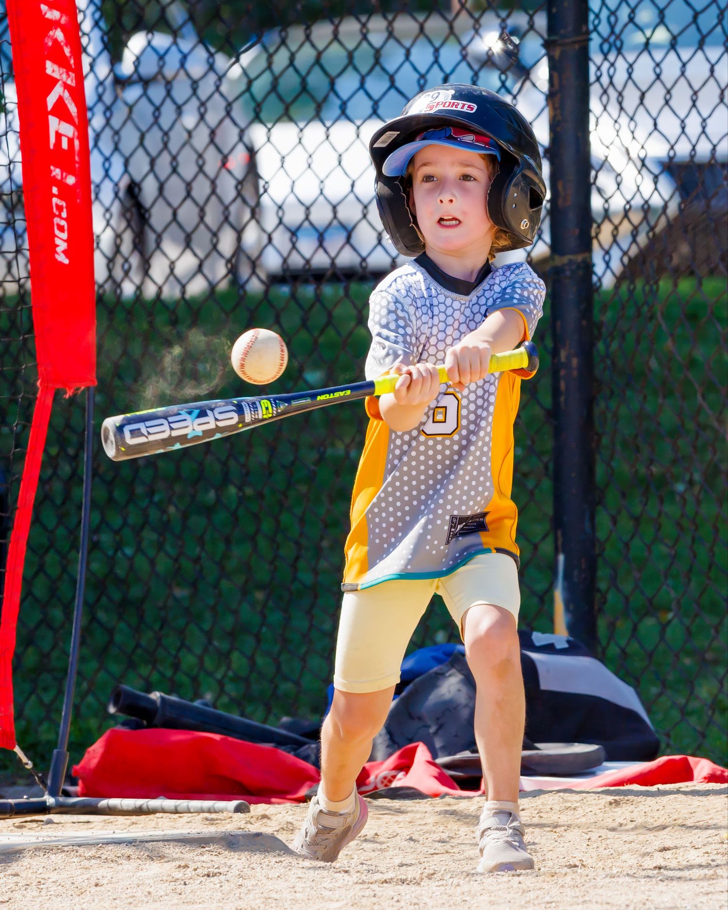 Young baseball player in yellow and gray uniform swings a bat at a ball during practice.