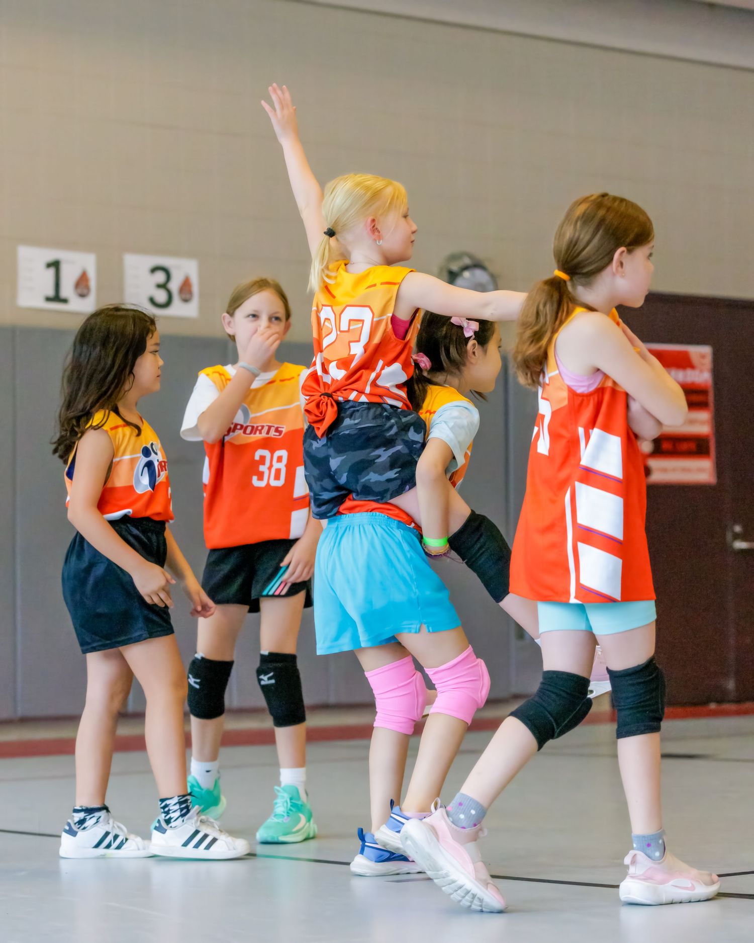 Group of young athletes performing synchronized lunges during indoor sports training session in colorful uniforms.