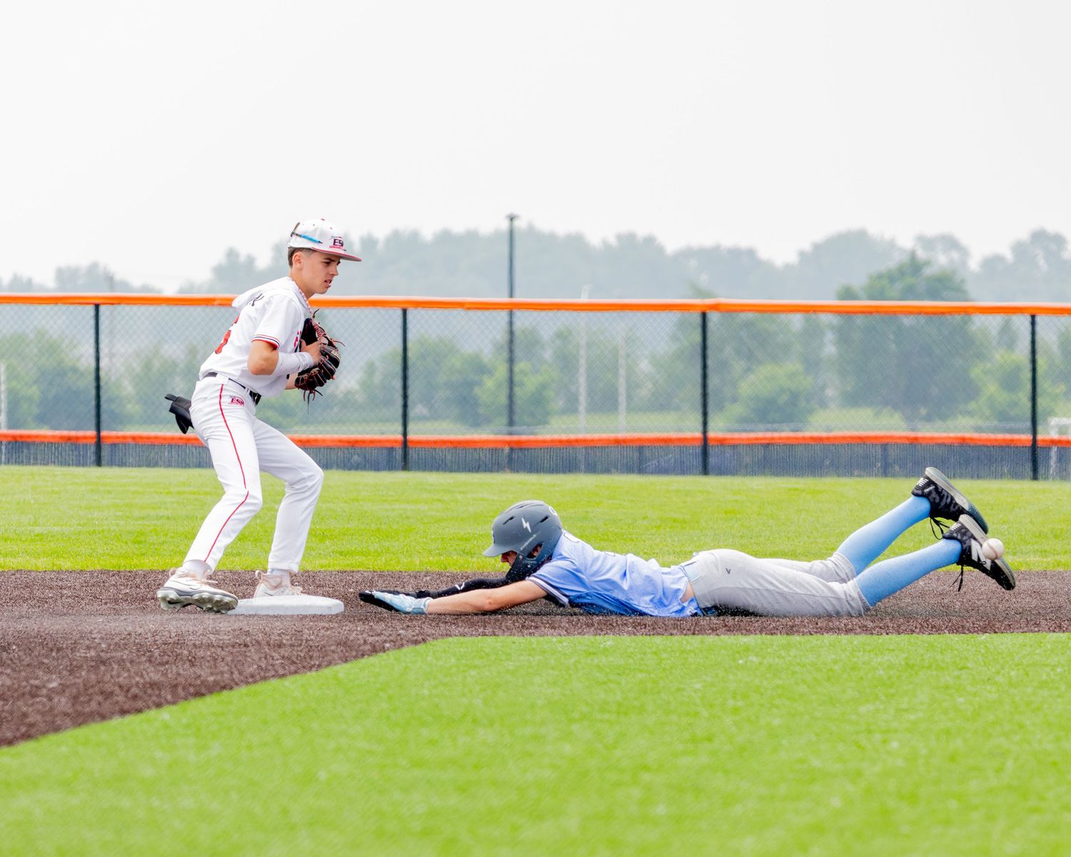 Baseball players slide into bases on a green field during competitive game action.