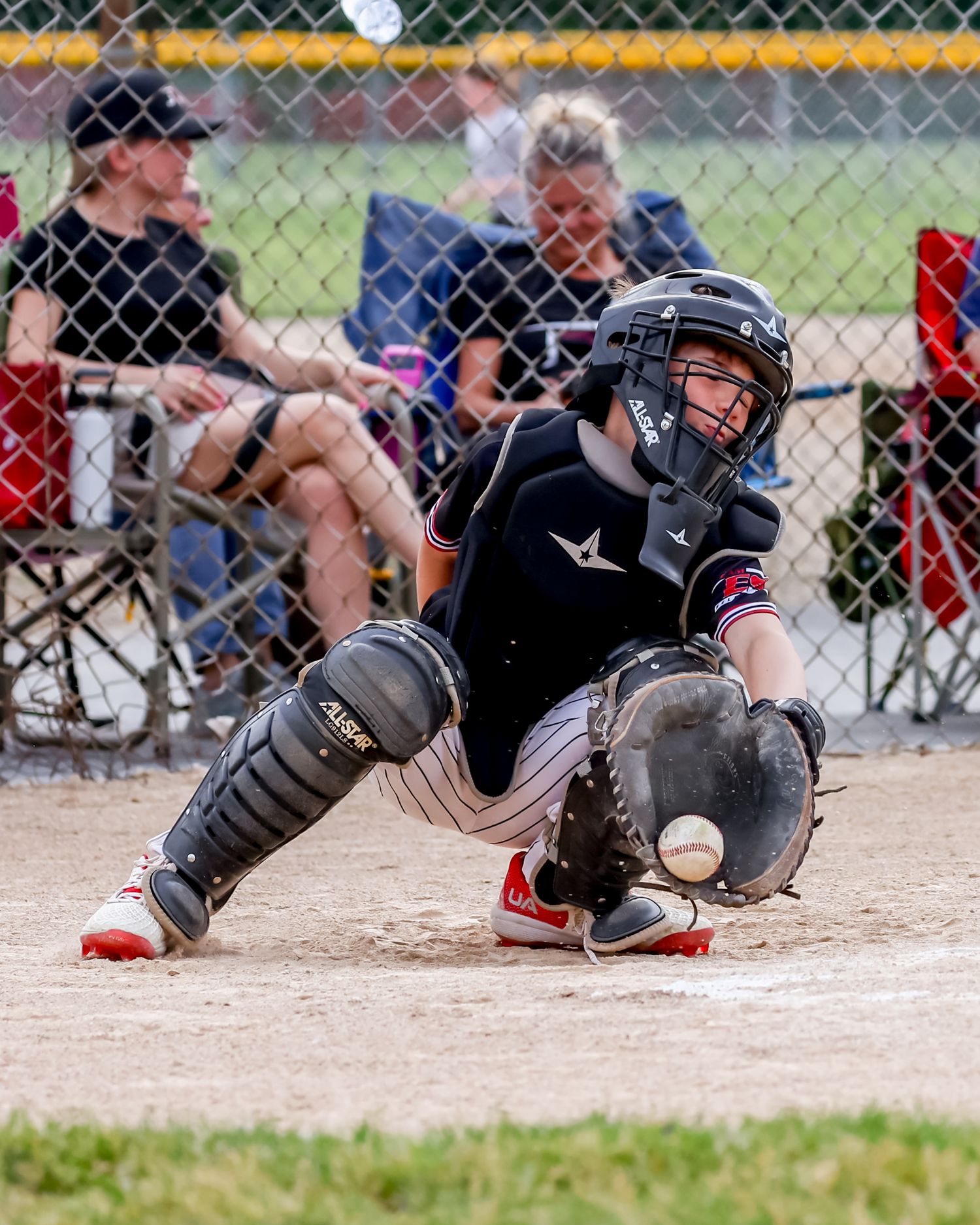 Baseball catcher in black gear sliding at home plate positioned to catch the ball during an intense play.