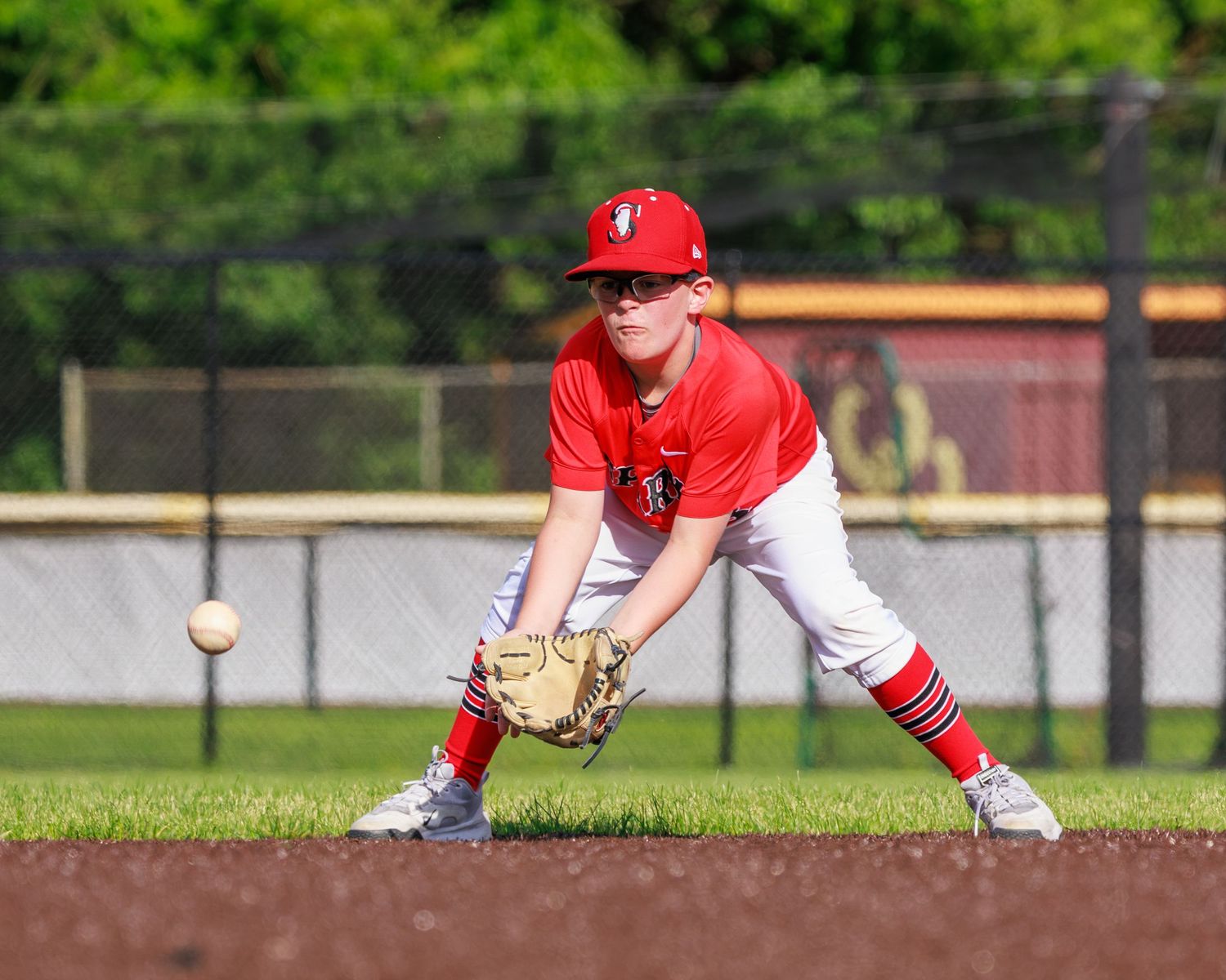 Young baseball player in red uniform fielding a ground ball on a sunny youth baseball diamond.
