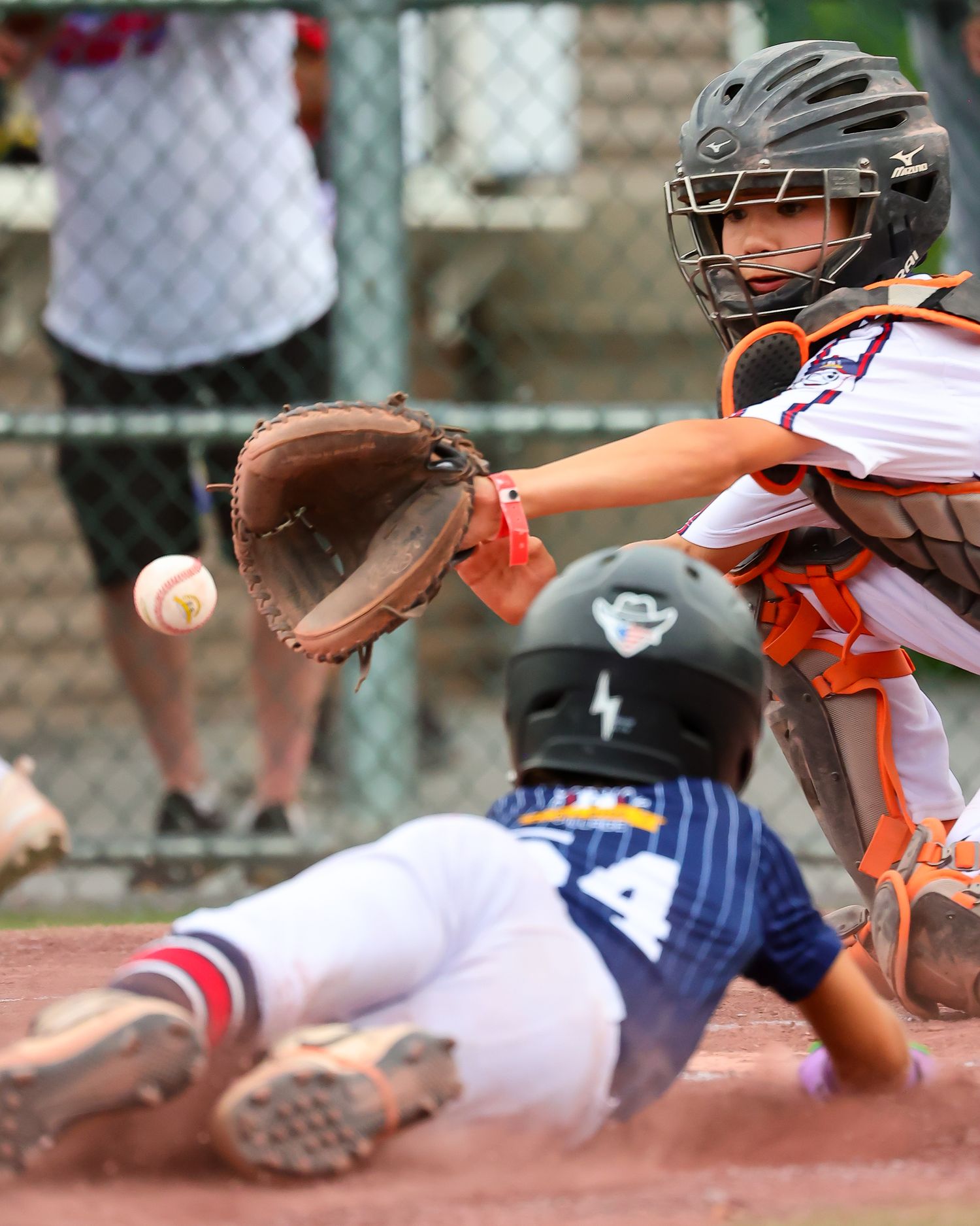 Baseball player slides into home plate during intense game action while catcher awaits the throw.