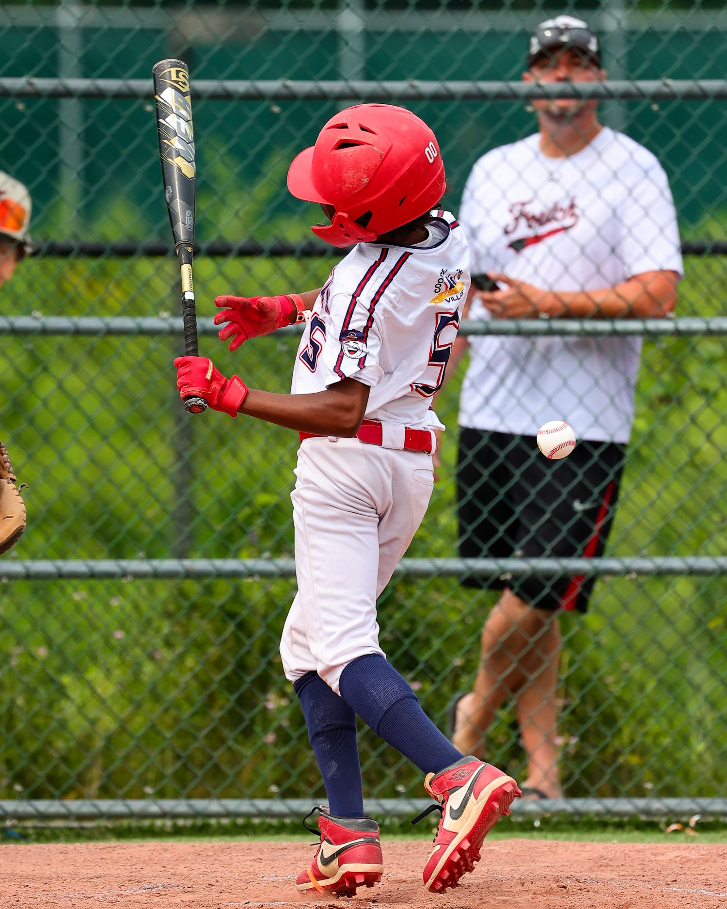 Baseball player in white uniform and red helmet takes a powerful swing at bat during a game.