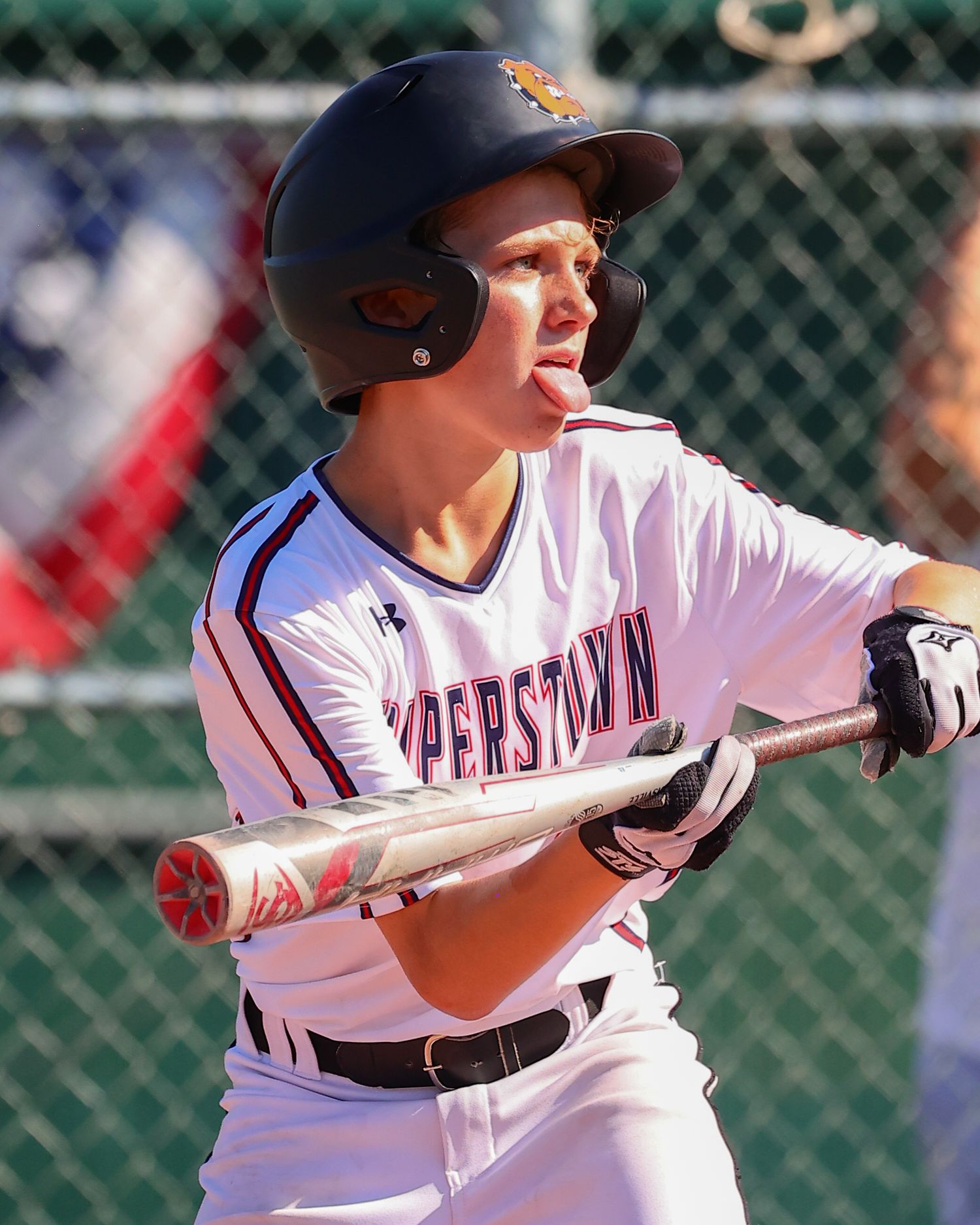 Baseball player in white uniform prepares to bunt during game with batting helmet and focused expression.