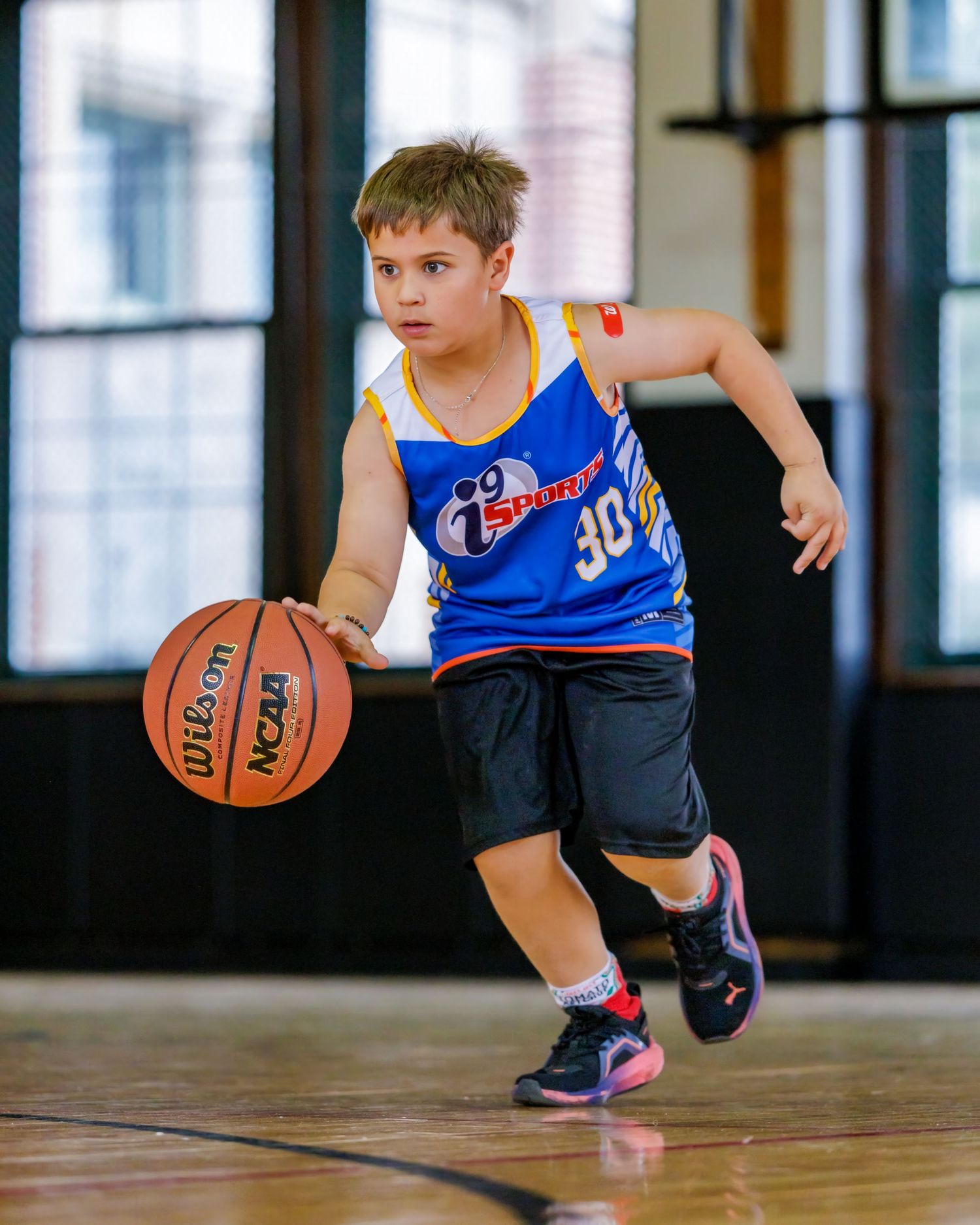 Young boy in blue jersey #30 dribbling basketball on indoor court during youth league game.